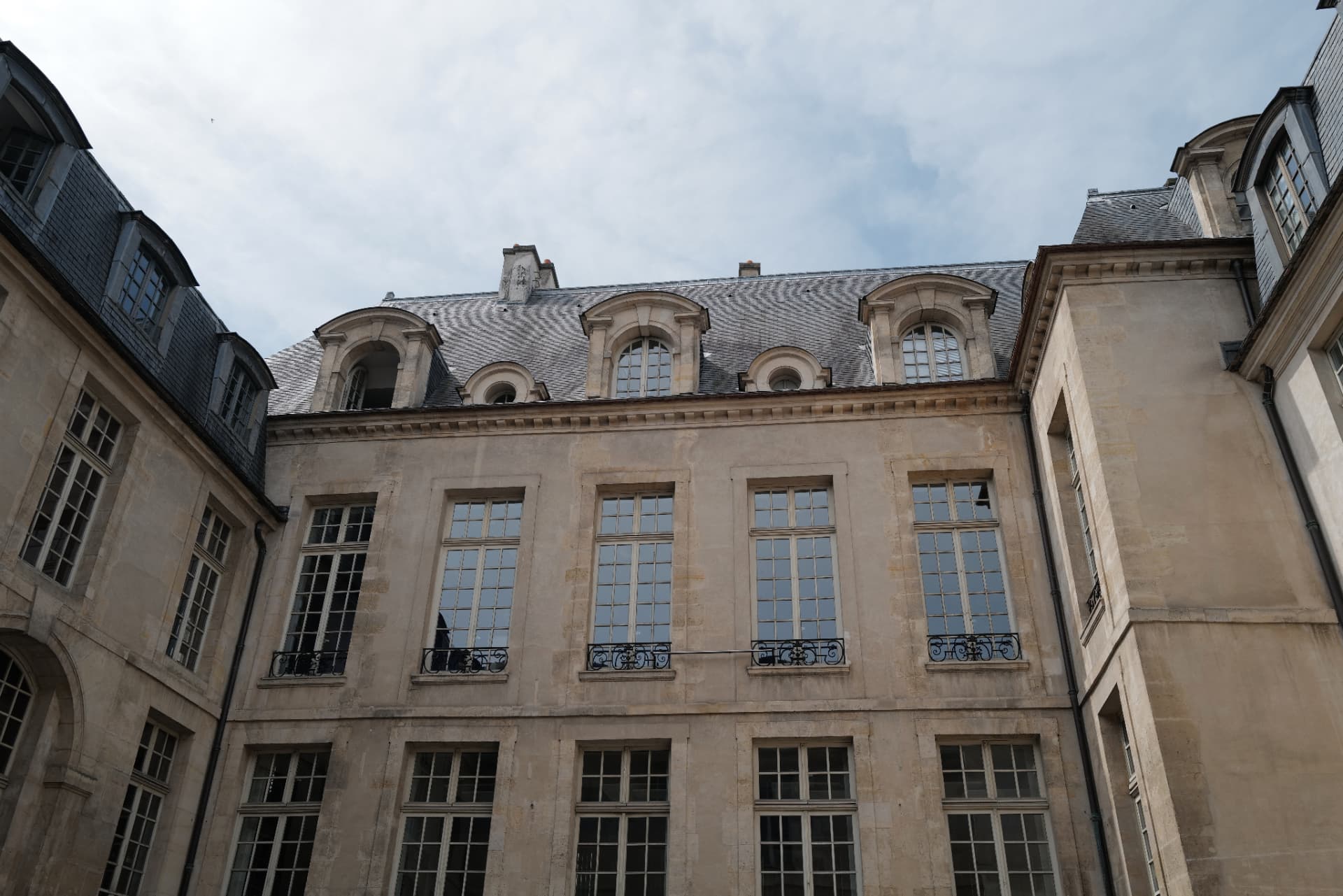 Classical stone courtyard façade with tall windows and slate dormer roofs in a Marais mansion