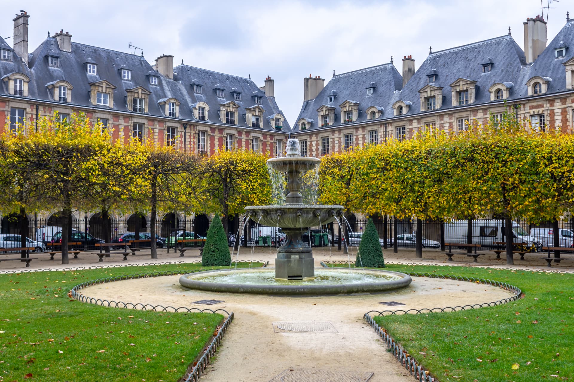 The central fountain of the Place des Vosges framed by autumn-coloured trees and arcaded brick façades