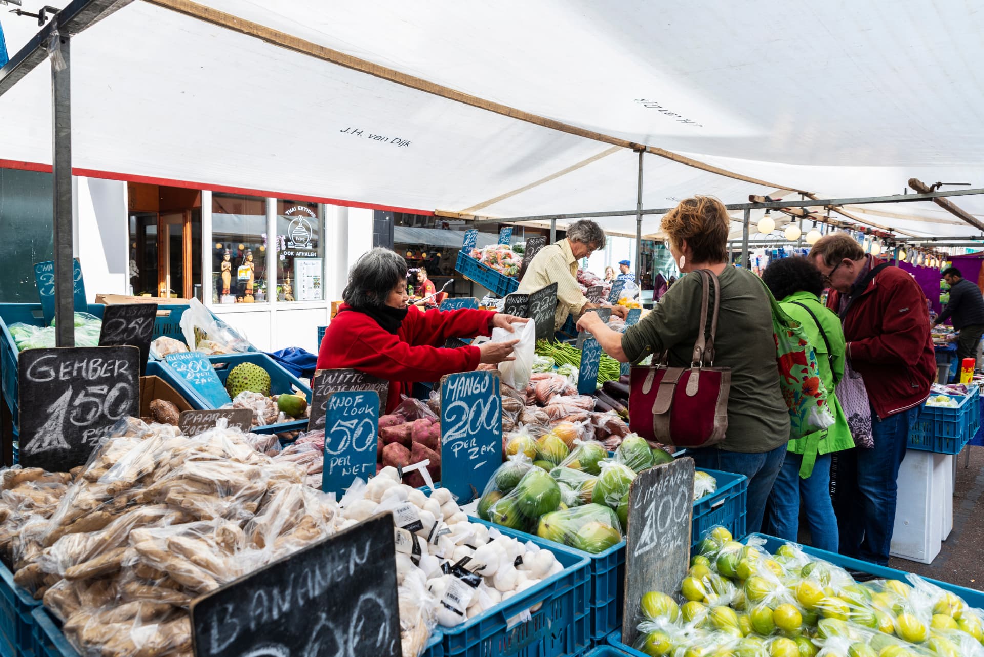 Shoppers at a fruit and vegetable stall at the Albert Cuyp Market in Amsterdam, with handwritten Dutch price boards
