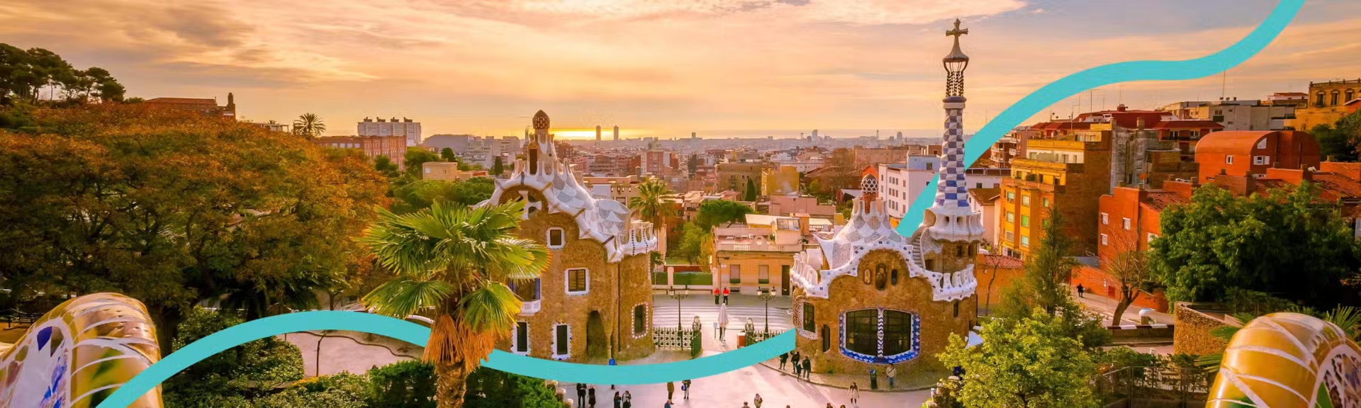 Panoramic view over Barcelona from Park Güell at sunset, with Gaudí's mosaic gatehouses, the city skyline and the Mediterranean coast