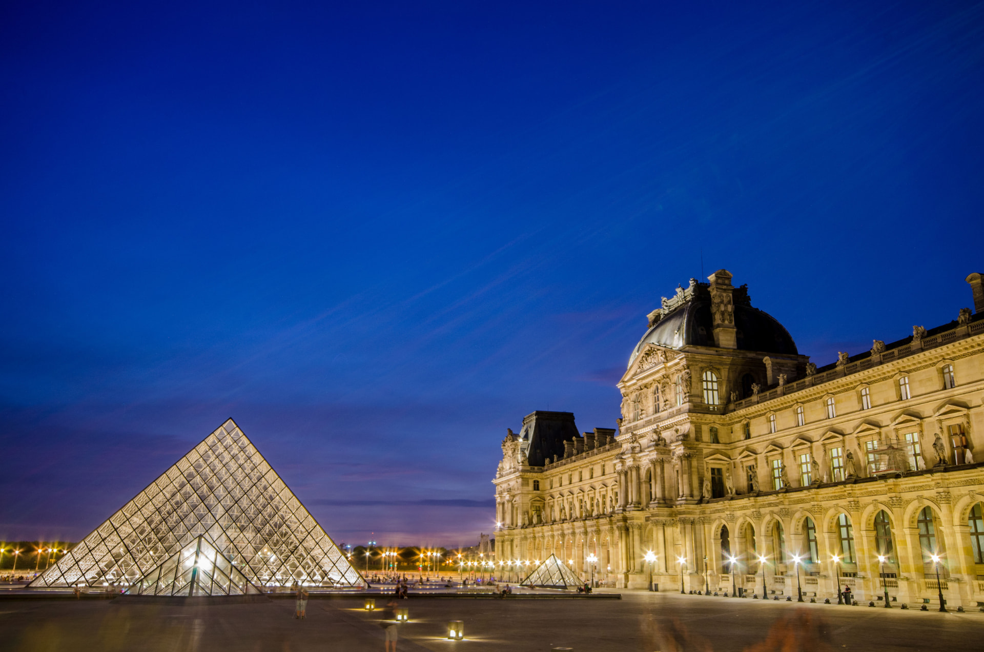 Illuminated glass pyramid and Louvre palace at dusk