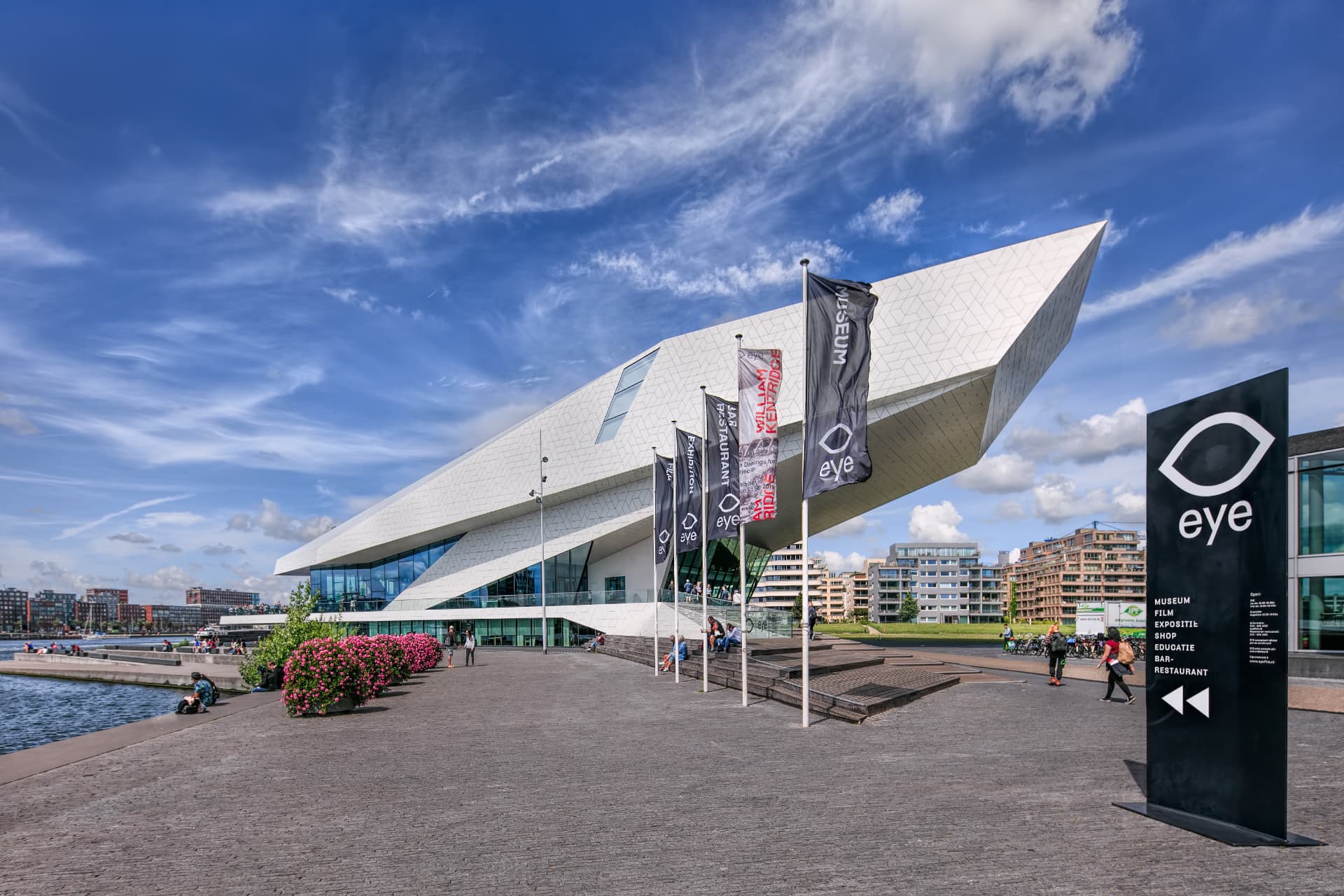 The angular white Eye Filmmuseum in Amsterdam with flags and the black eye sign on the waterfront square