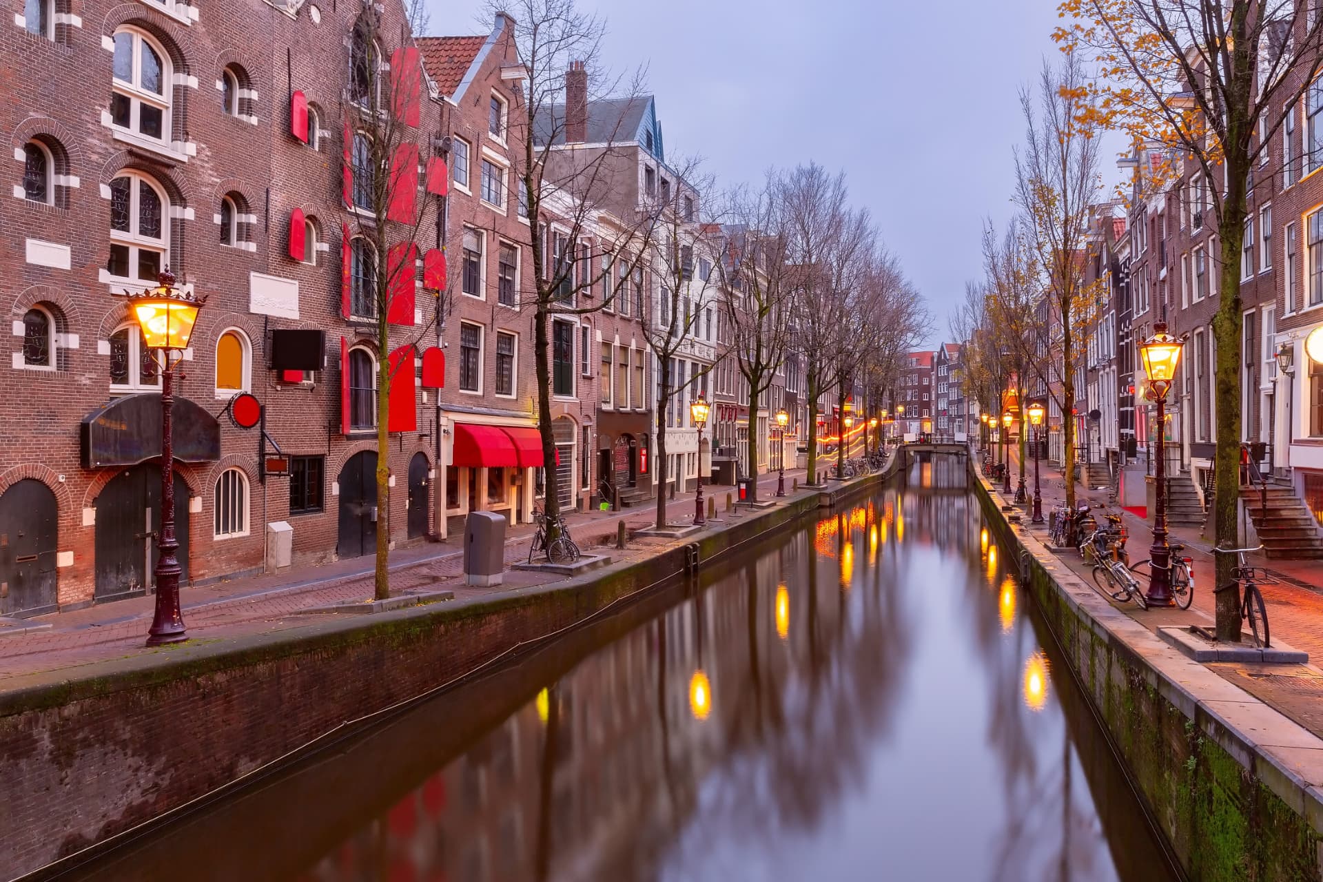Quiet canal in De Wallen at dusk with lit street lamps and canal houses