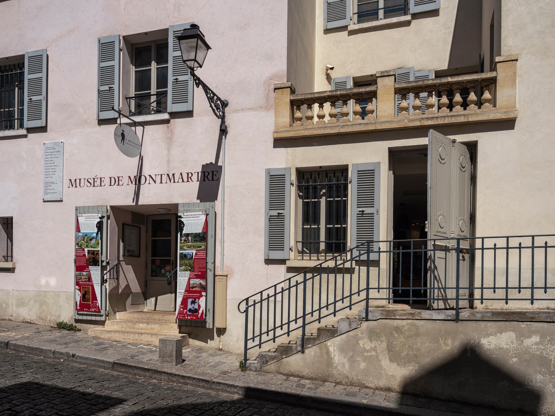 The entrance of the Musée de Montmartre on rue Cortot, with shutters, a street lamp and exhibition posters
