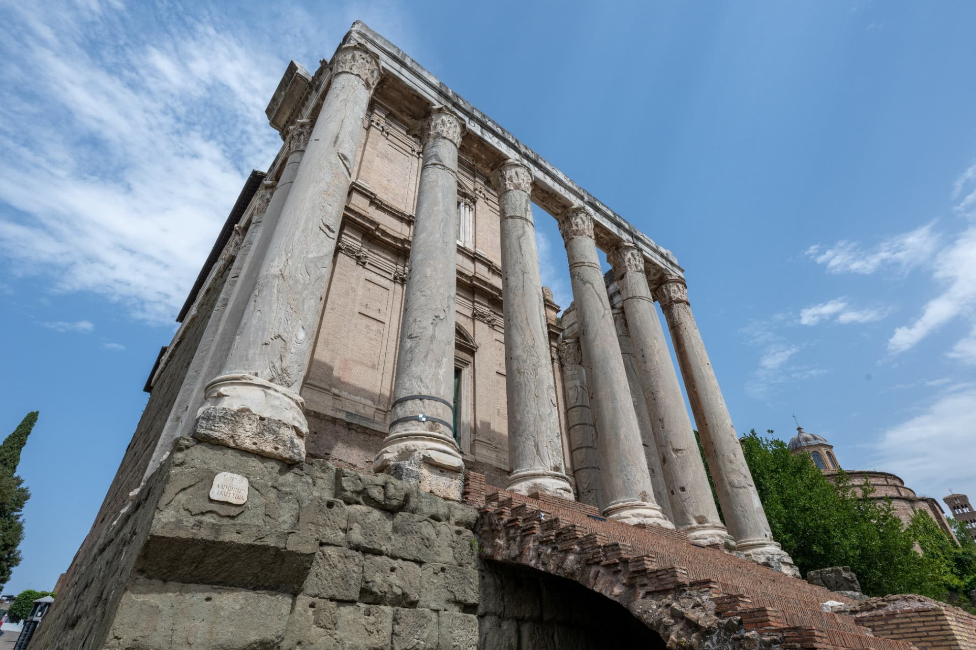 Low-angle side view of the Temple of Antoninus and Faustina showing its tall marble columns and stone podium
