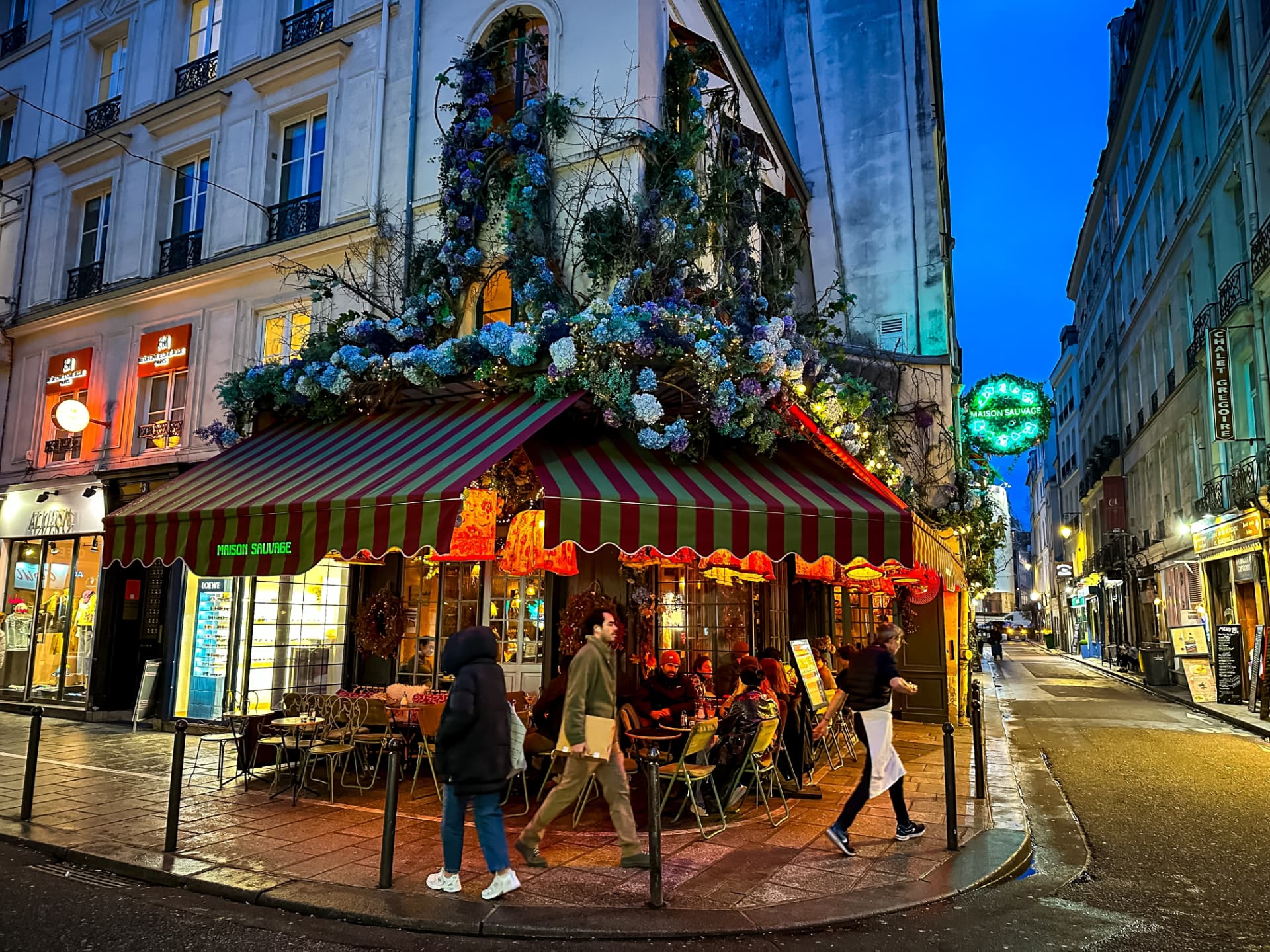 The flower-covered facade of a café on a Saint-Germain-des-Prés street corner at night