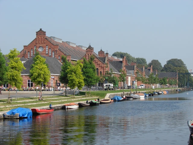 The red-brick Westergas buildings beside a canal with small boats and young trees in Westerpark, Amsterdam