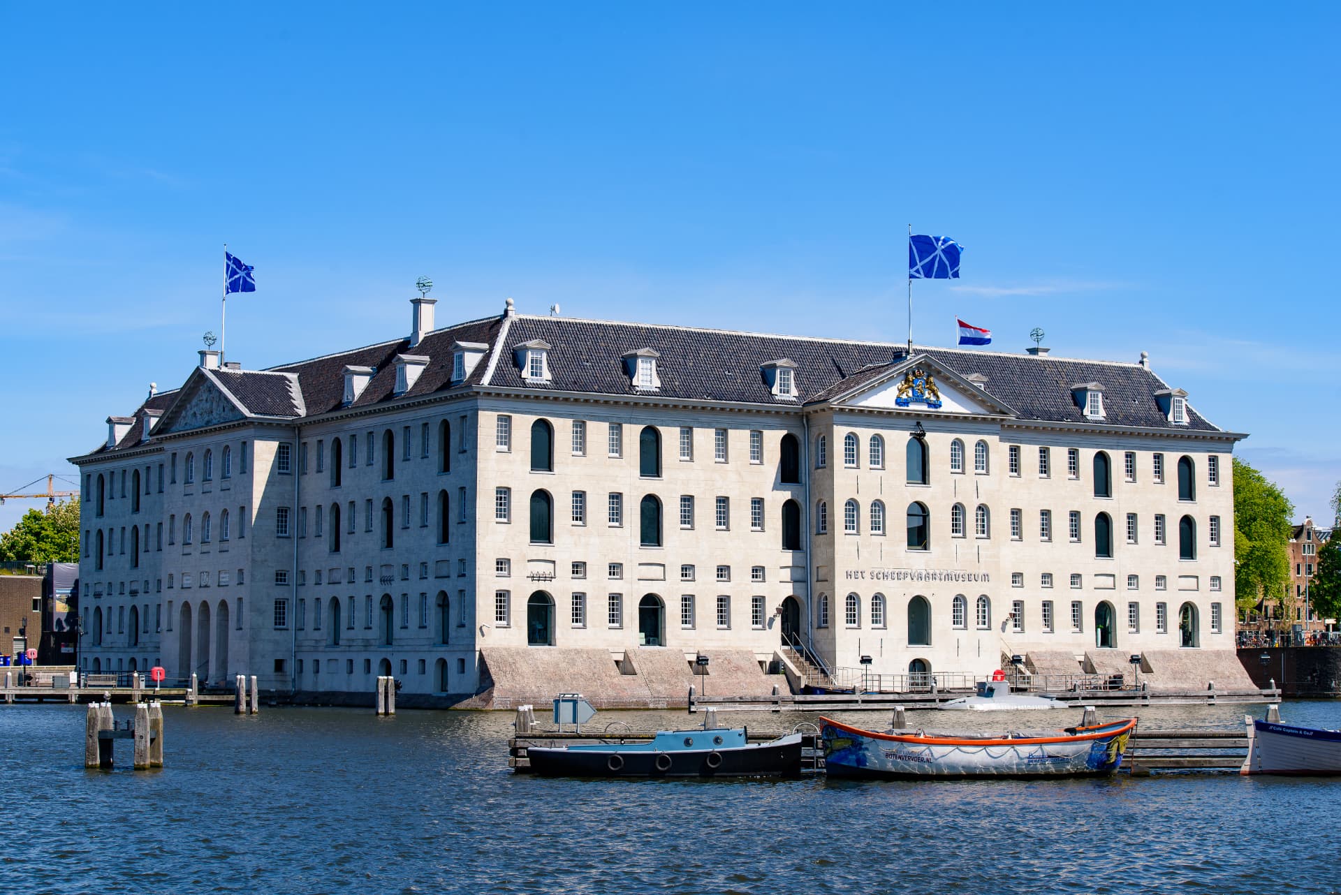 The National Maritime Museum in Amsterdam on a clear day with small boats moored in the foreground