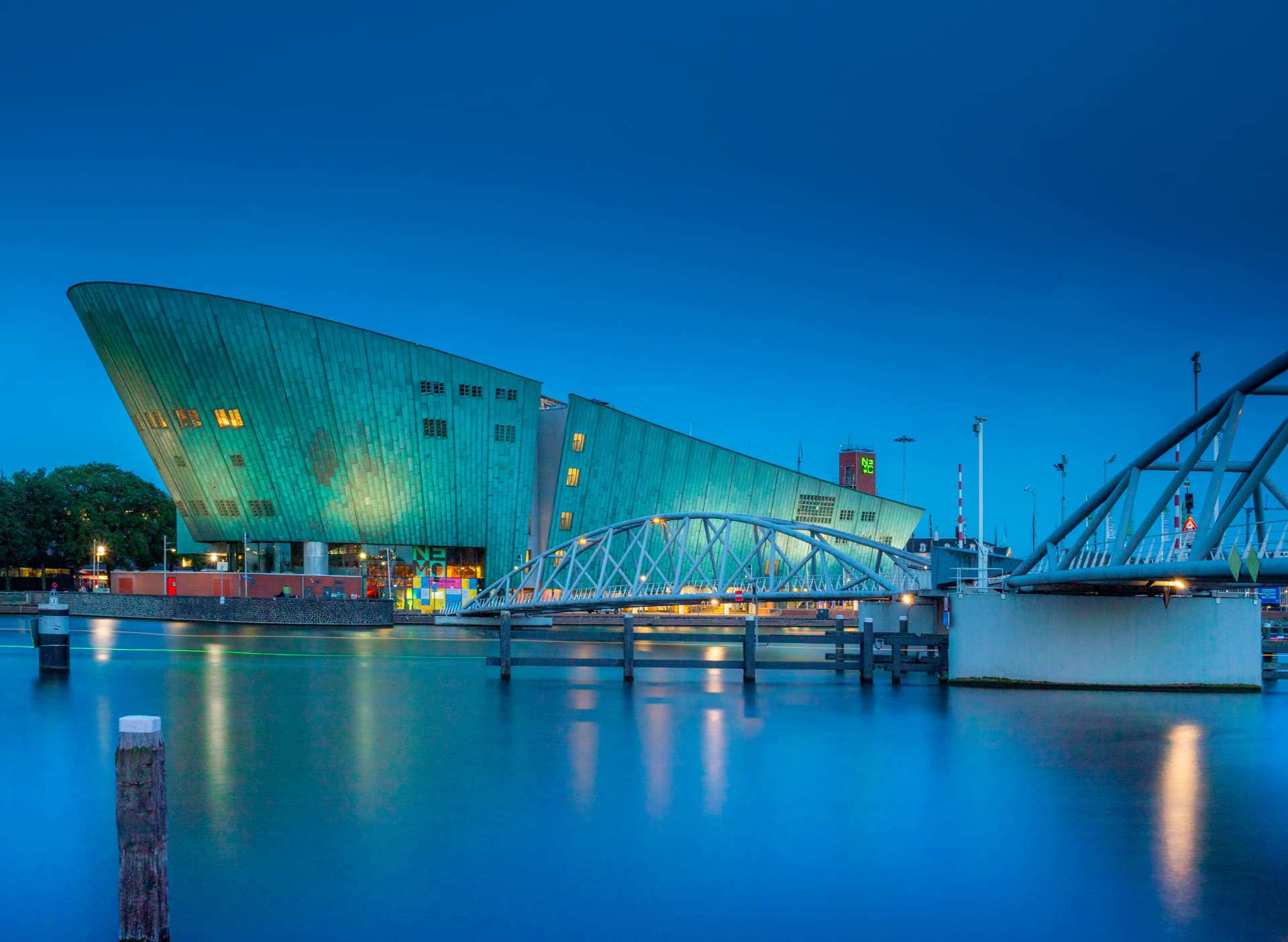 The NEMO Science Museum in Amsterdam at dusk with its green copper facade reflected in the calm harbour