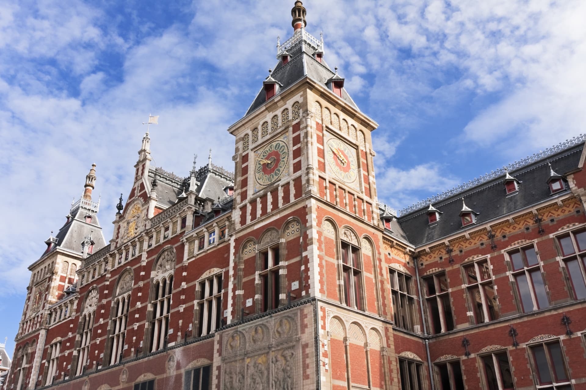 Clock tower of Amsterdam Centraal Station with red brick, gilded clock faces and painted shields