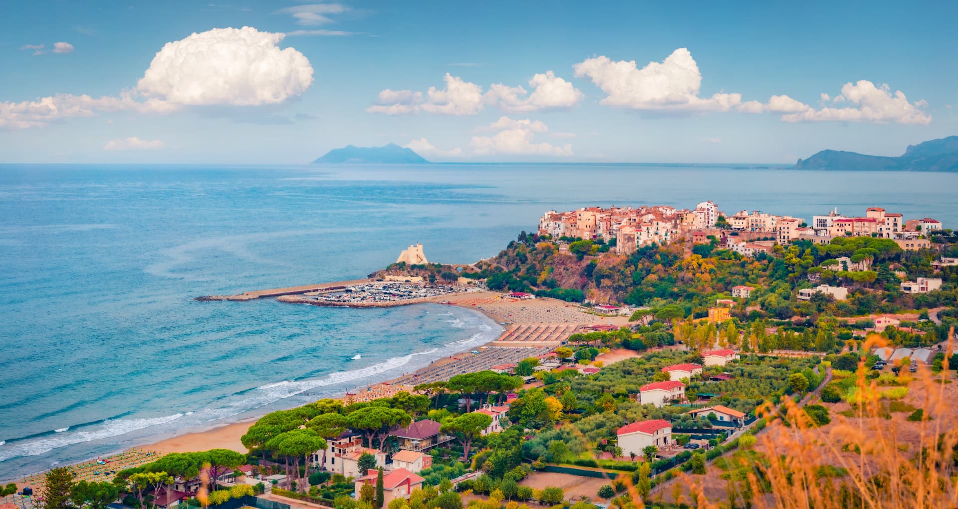 Aerial view of Sperlonga's whitewashed old town on a headland above a long sandy beach and turquoise sea