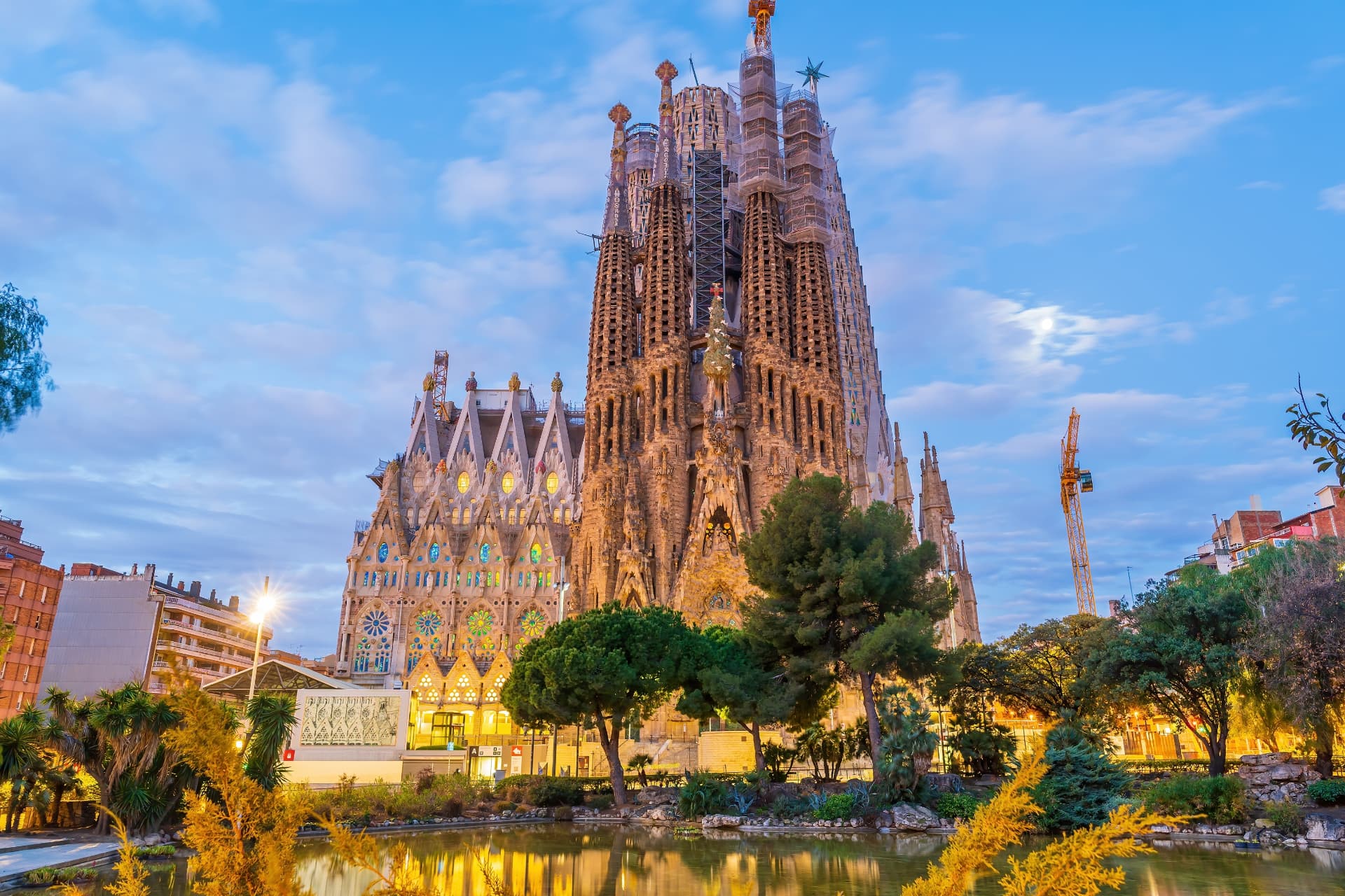 The Sagrada Família illuminated at dusk, reflected in the pond of Plaça de Gaudí