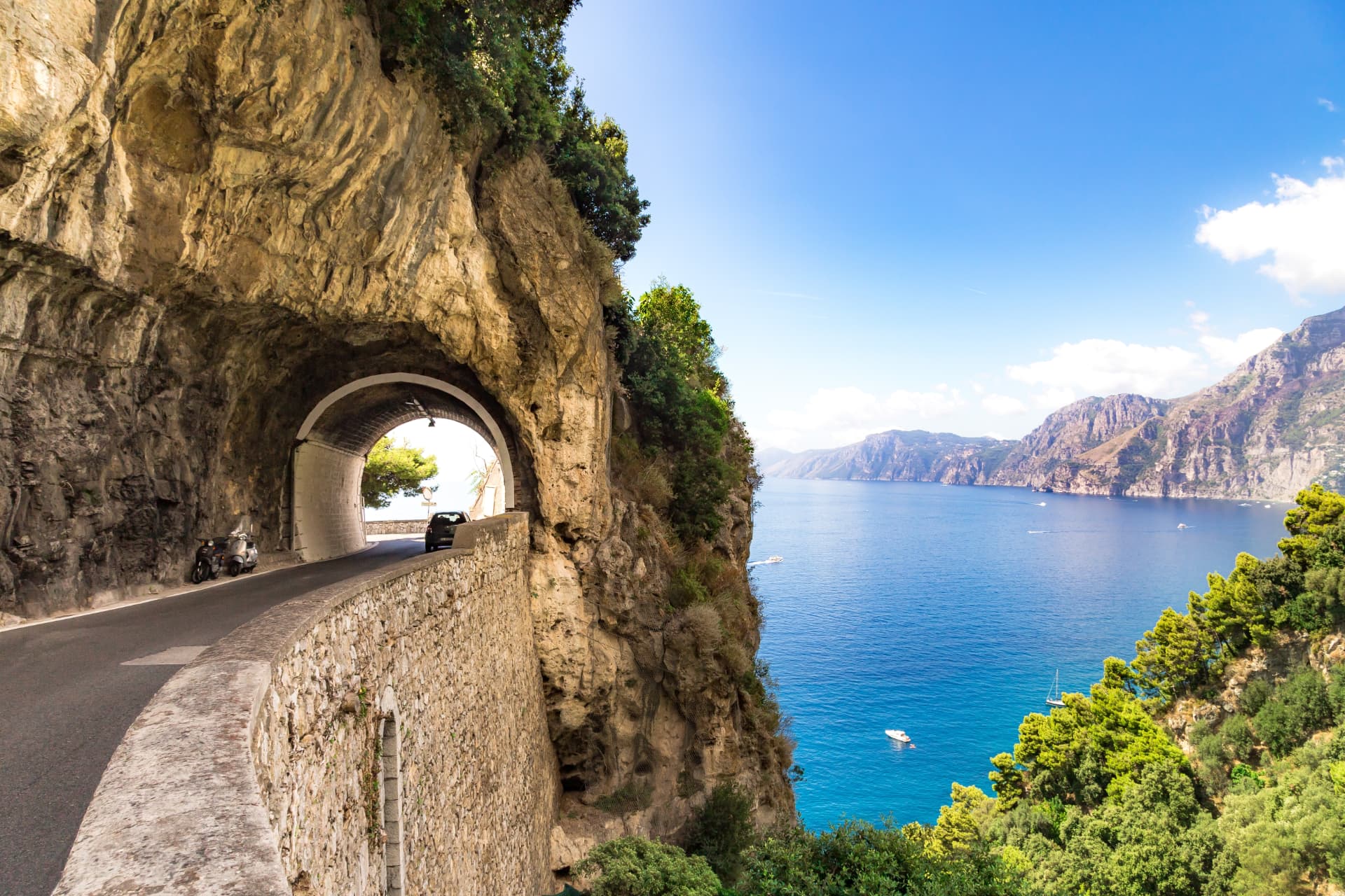 A tunnel carved through the cliff on the SS163 Amalfi Coast road, with the sea and headlands beyond