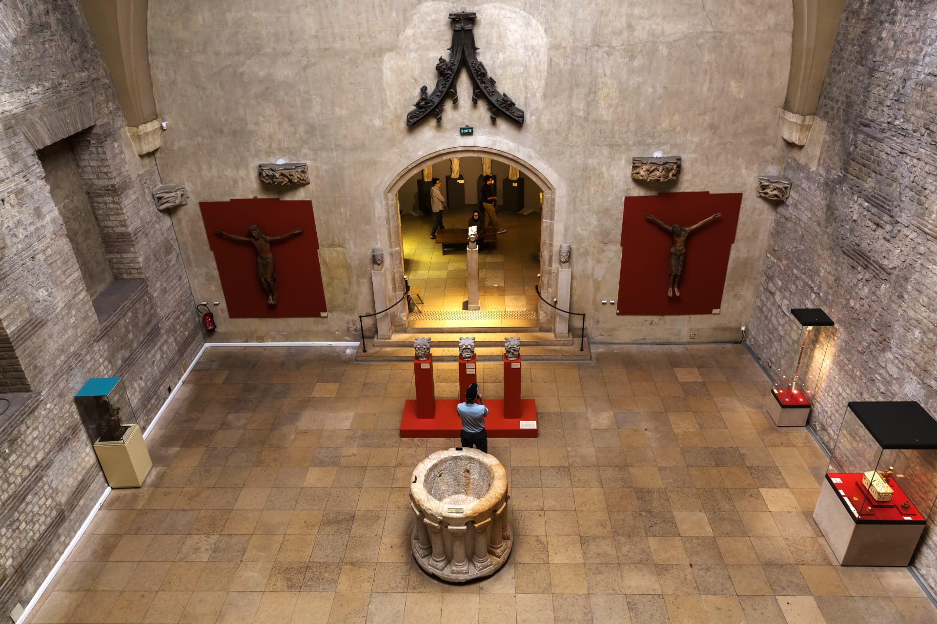 The vaulted Roman frigidarium of the Thermes de Cluny displaying medieval sculpture on red panels
