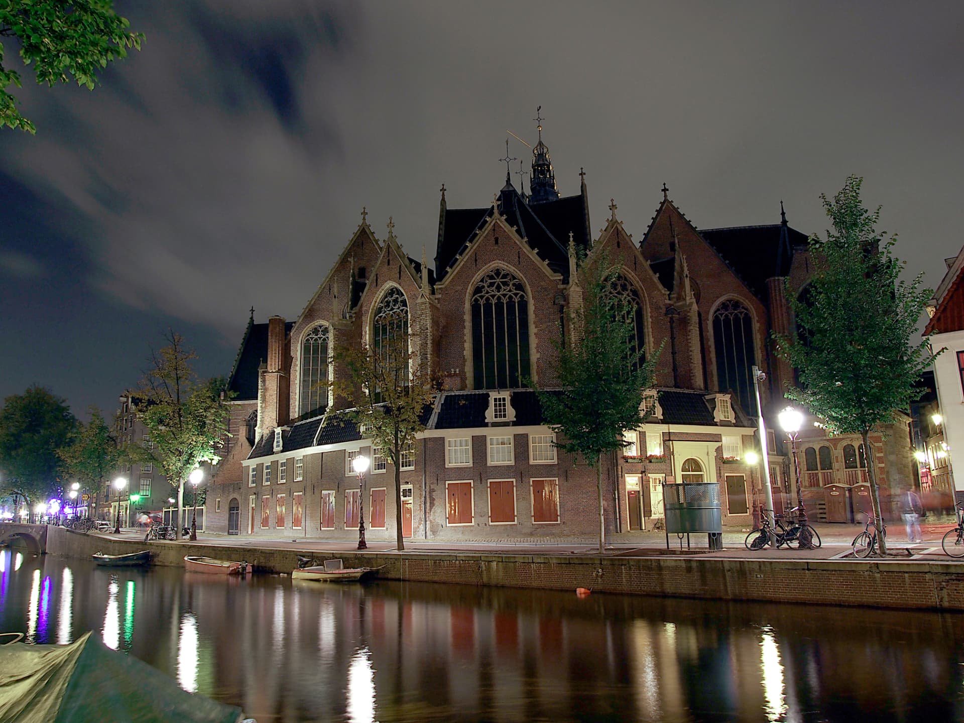 The Oude Kerk lit by street lamps at night, reflected in the canal