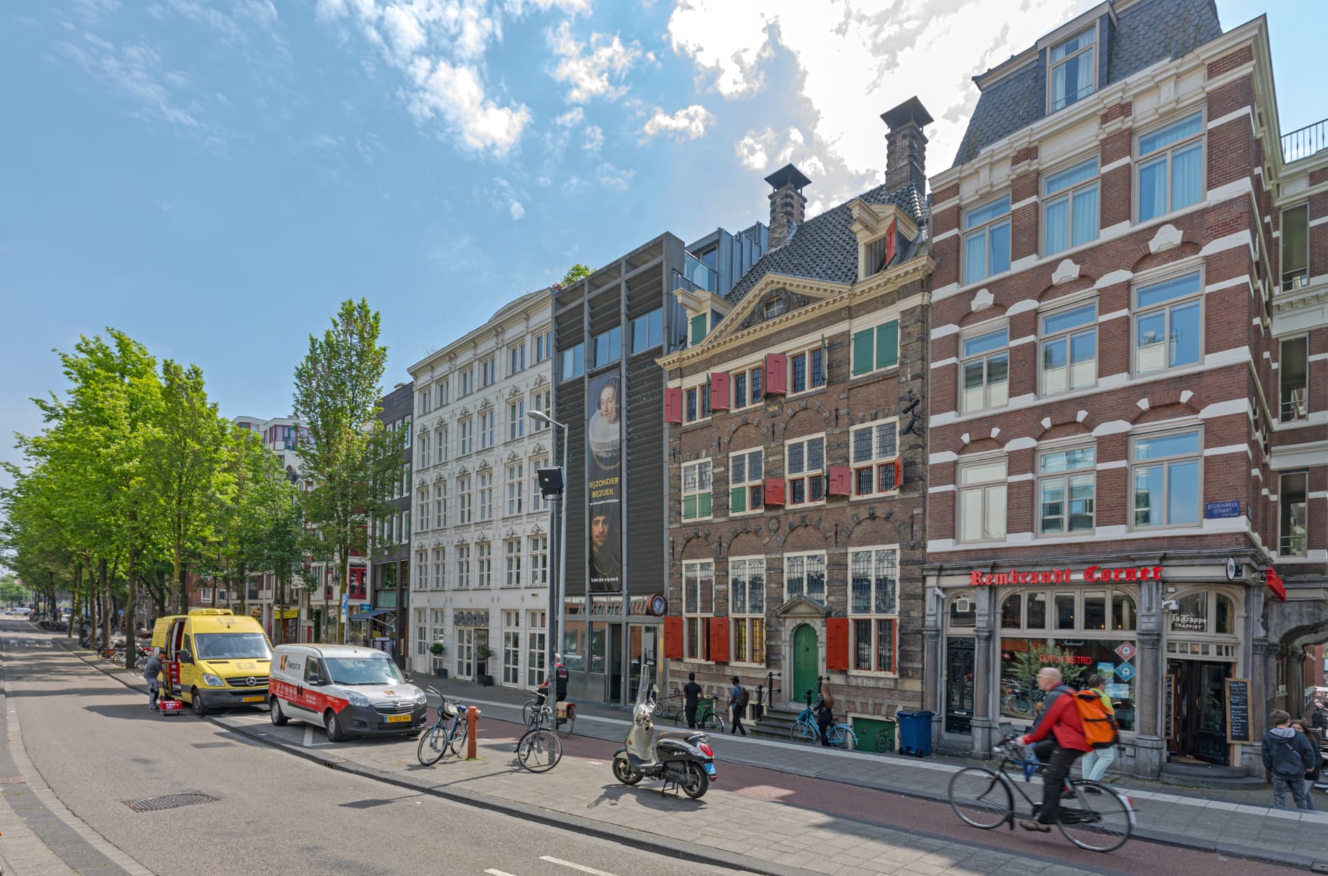 The Rembrandt House Museum on the Jodenbreestraat in Amsterdam, a 17th-century brick house with red and green shutters beside the modern museum entrance