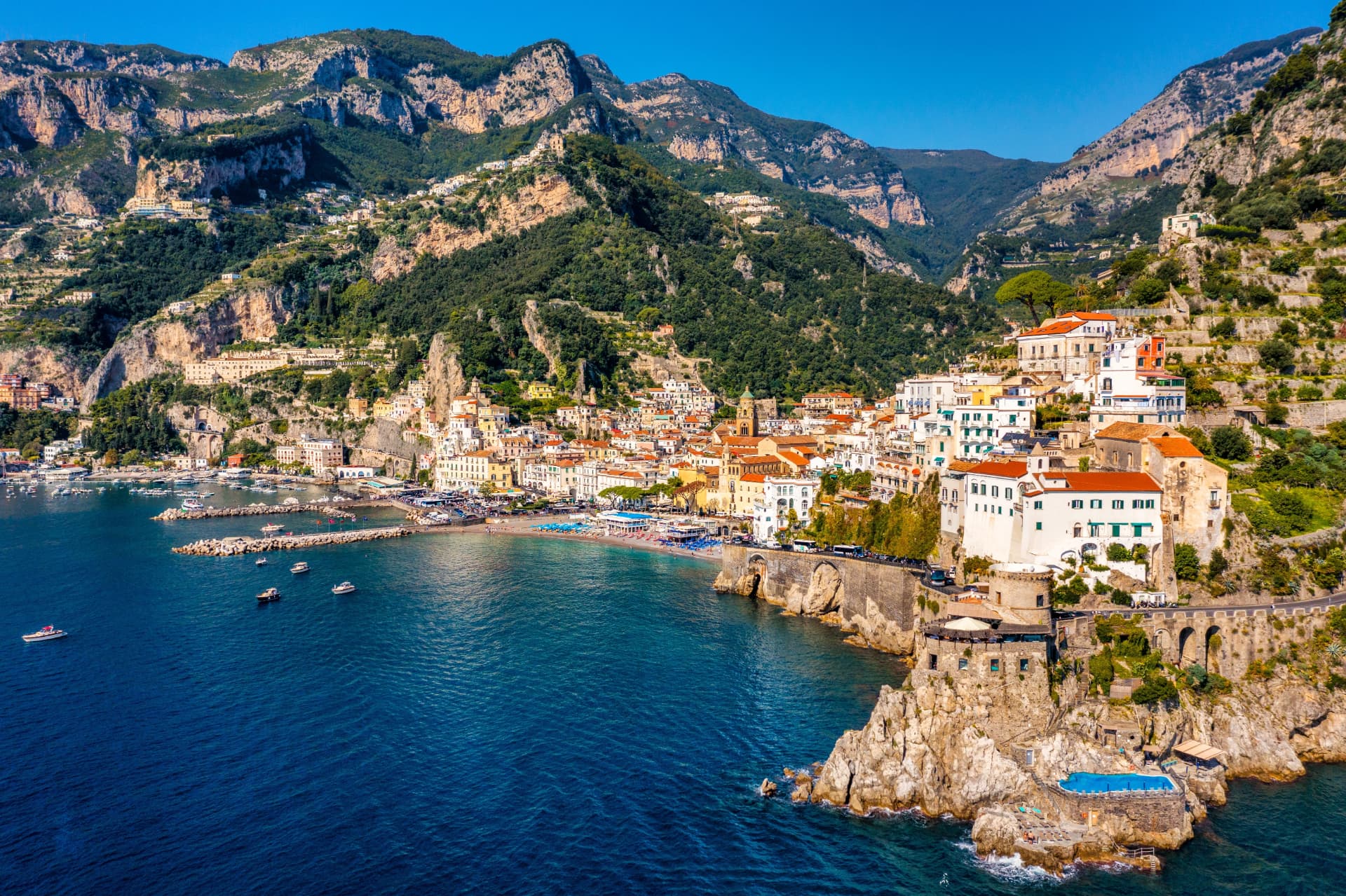 Aerial view of Amalfi's harbour, beach and cliffside town beneath the mountains of the Amalfi Coast