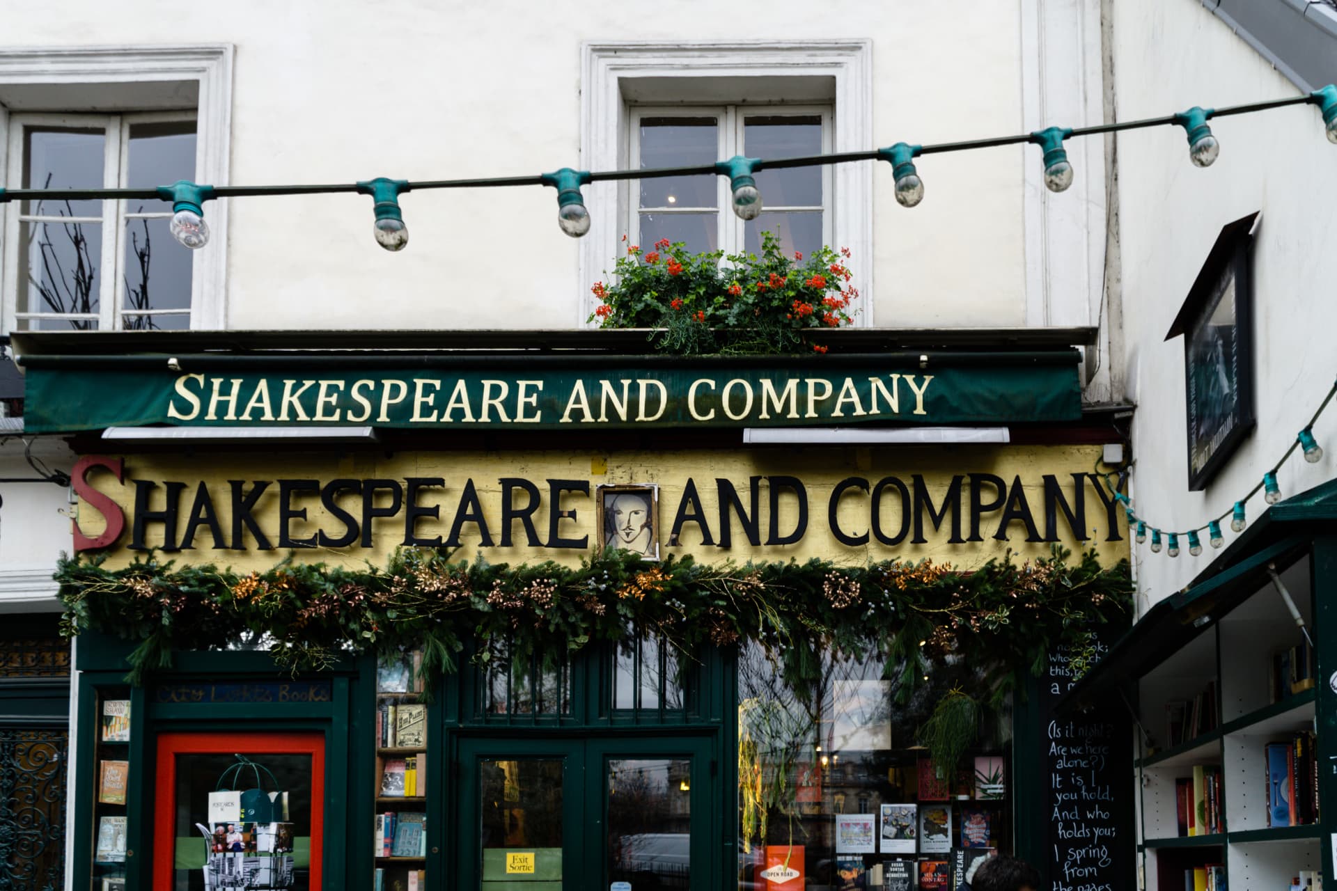 Close-up of the green Shakespeare and Company sign with its Shakespeare portrait plaque
