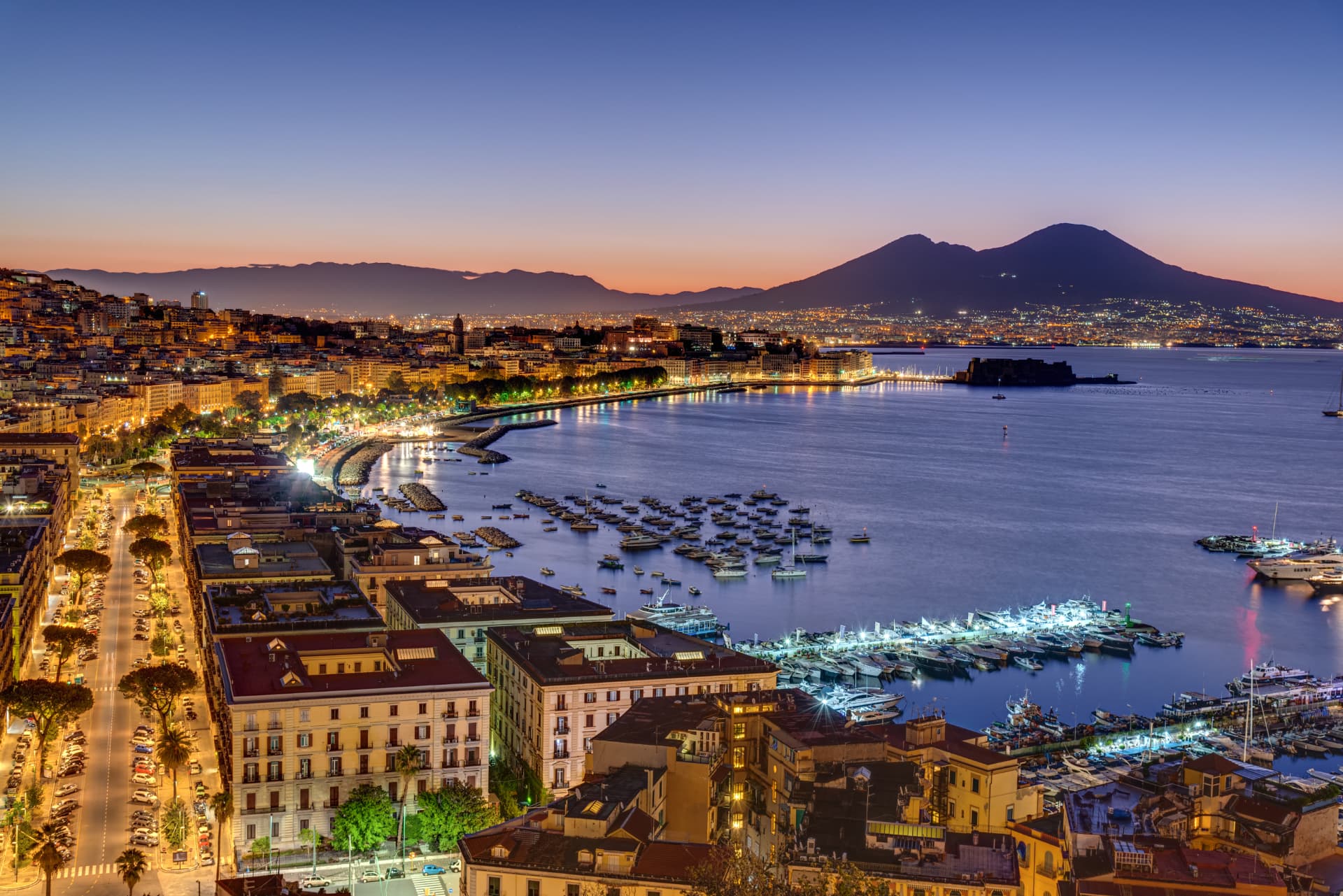 Panorama of Naples at dusk with the illuminated waterfront, the bay and Mount Vesuvius in the background