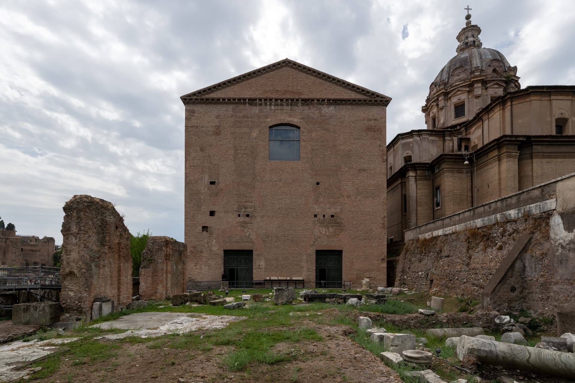 Tall brick facade of the Curia Julia, the Senate House in the Roman Forum, under a cloudy sky
