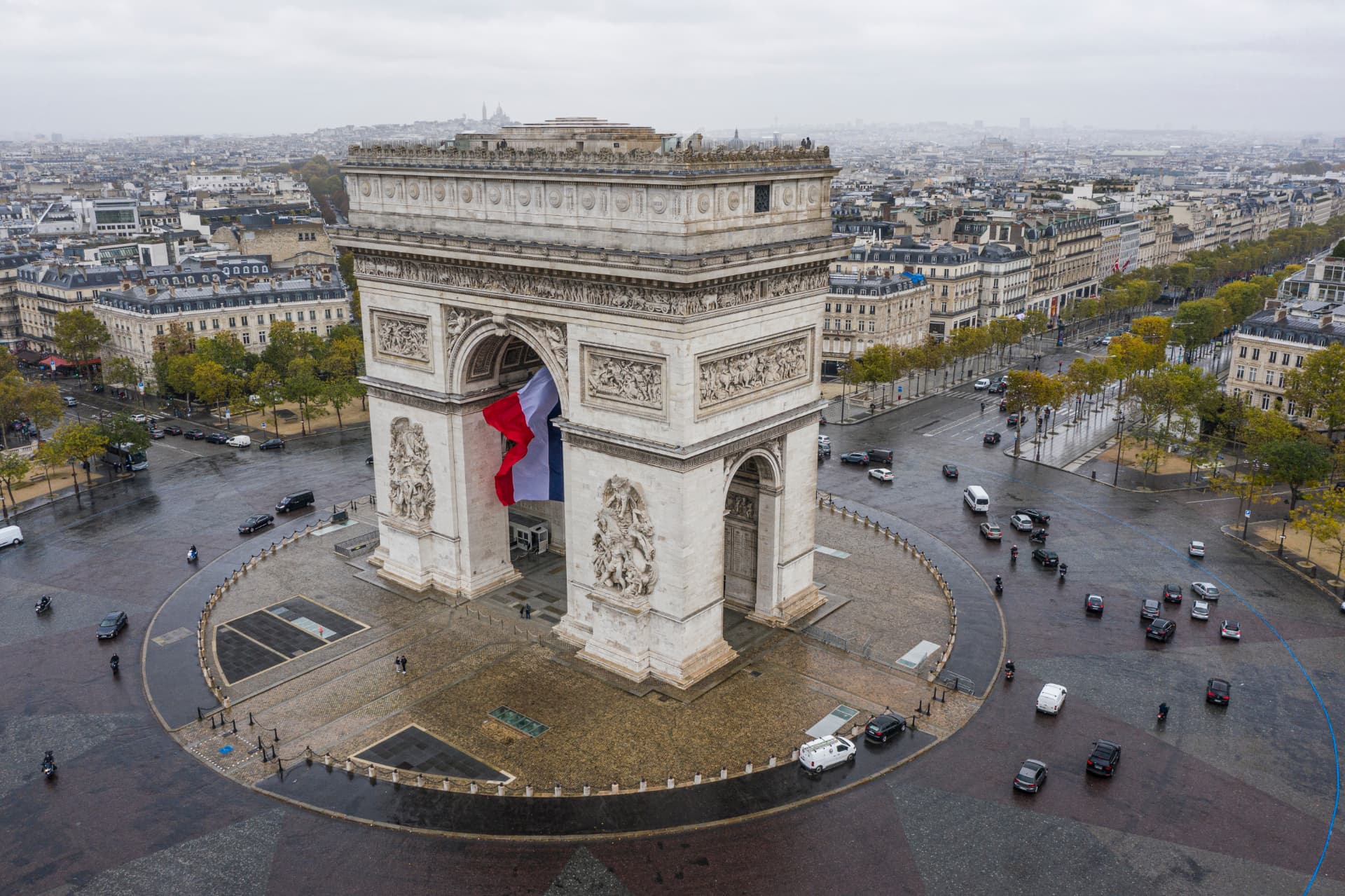 Aerial view of the Arc de Triomphe with a French flag beneath its arch