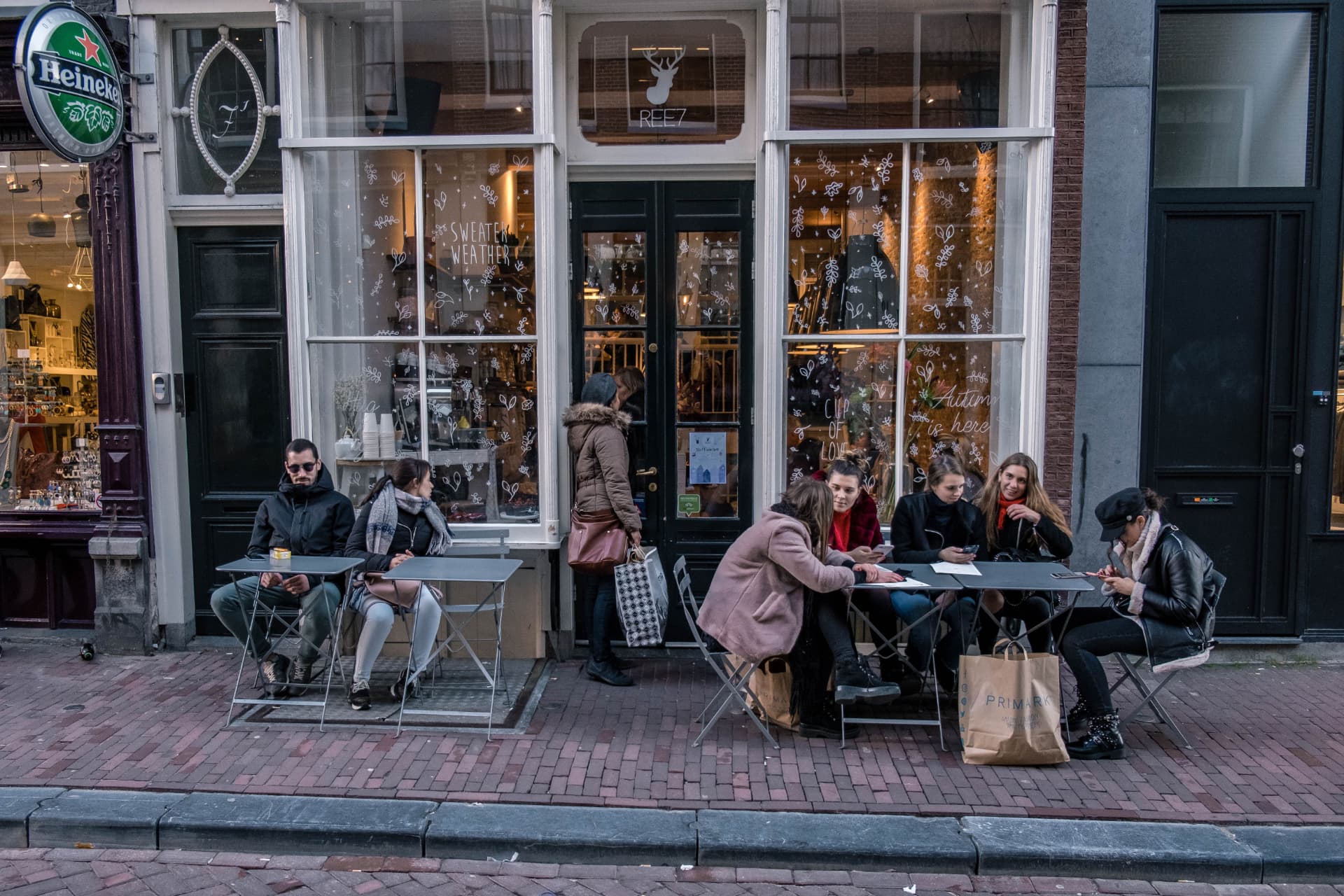 People at outdoor café tables on a brick-paved street in Amsterdam's 9 Streets shopping district