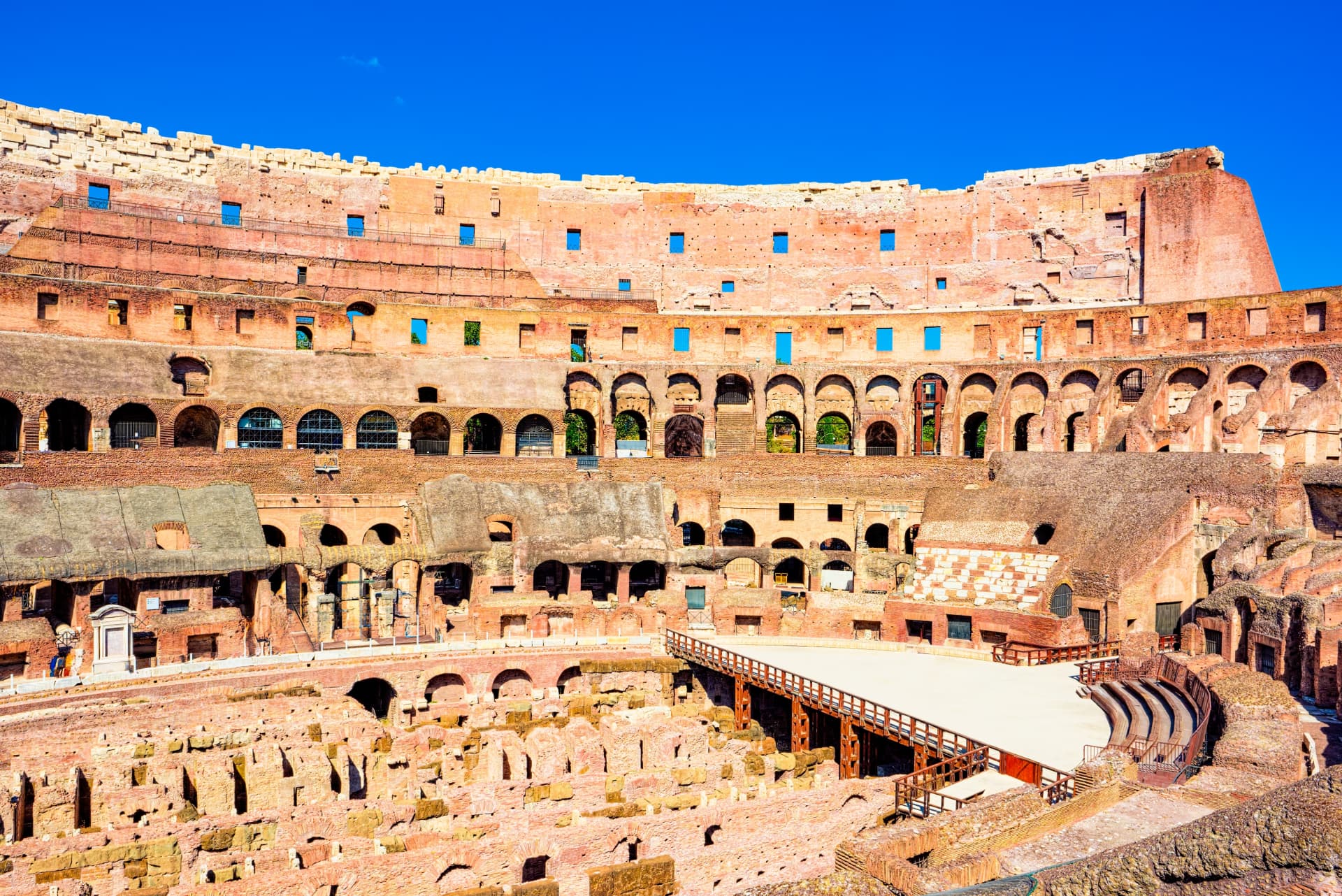 Interior view of the Colosseum showing the wooden arena floor, the exposed underground hypogeum walls and the seating tiers above