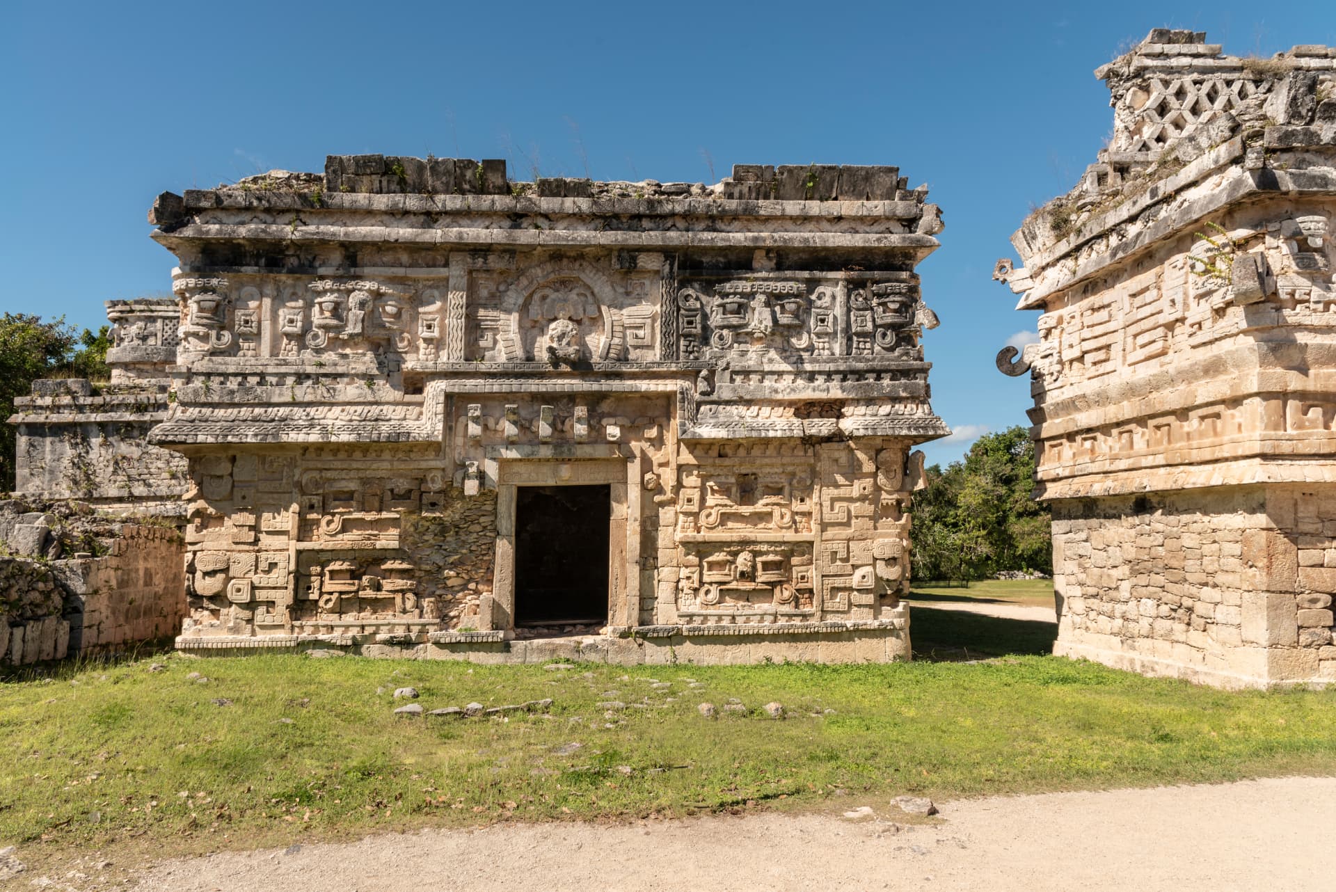 Detailed Maya stone carvings on buildings at Chichén Itzá under a clear blue sky