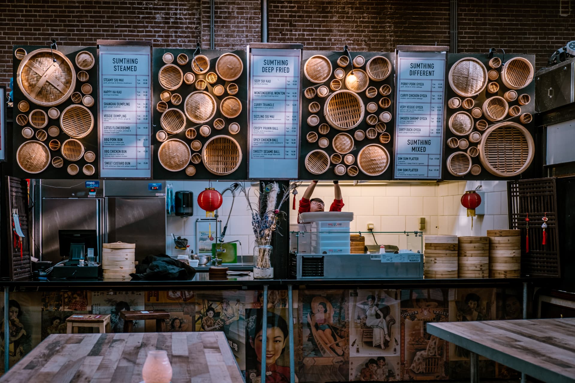 A dim sum stall at Foodhallen with menus between bamboo steamer baskets and vintage posters on the counter