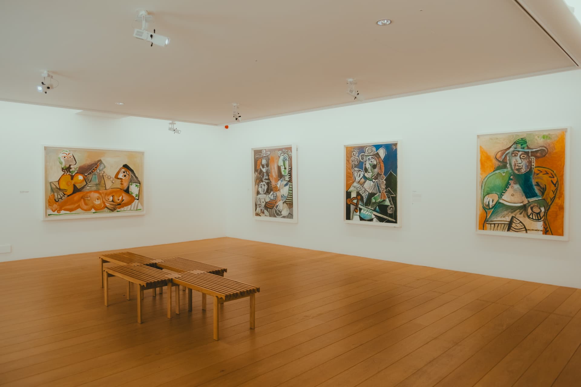 A bright white gallery room with large Picasso paintings and wooden benches at the Musée Picasso Paris
