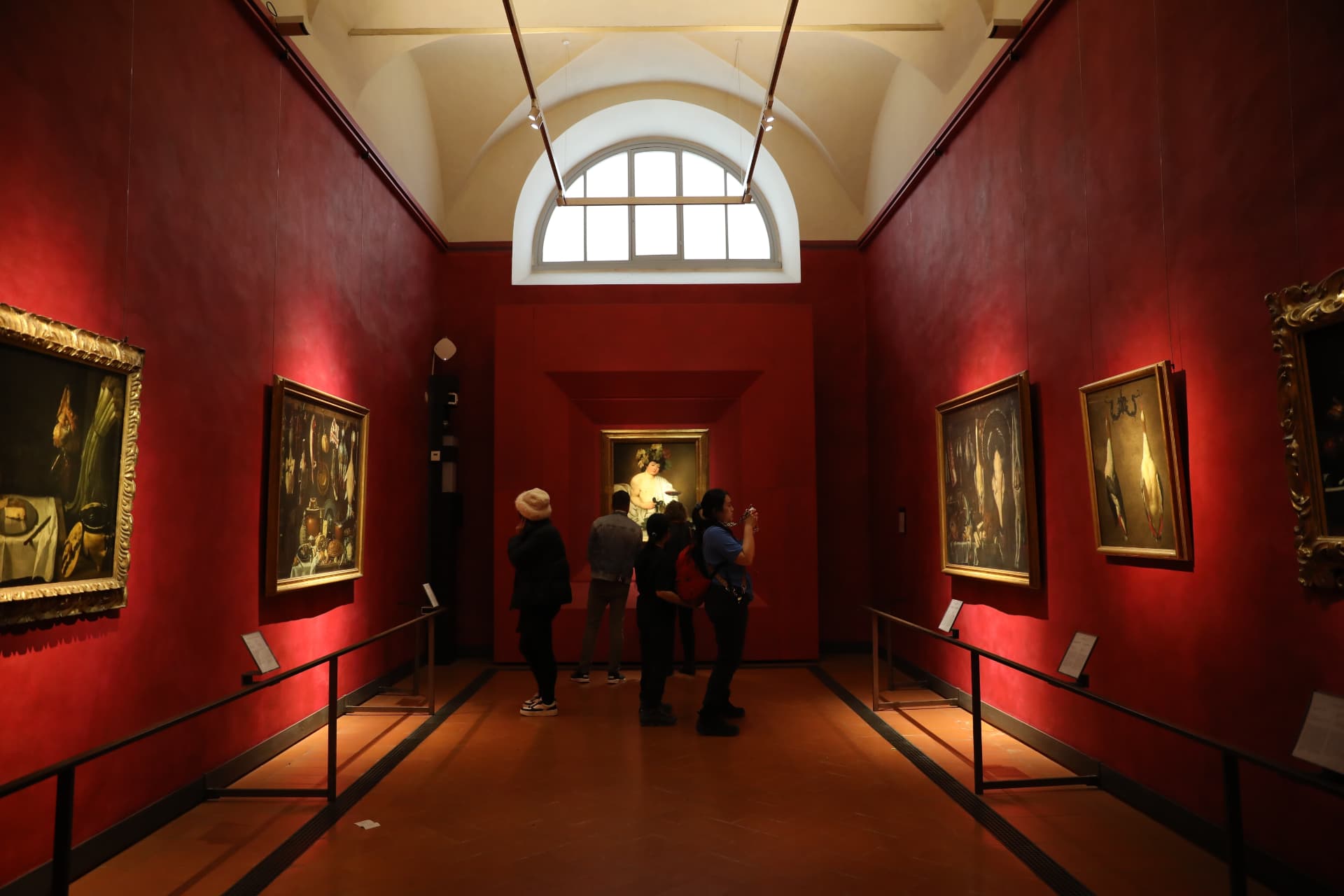 Visitors looking at paintings in a red-walled Uffizi exhibition room