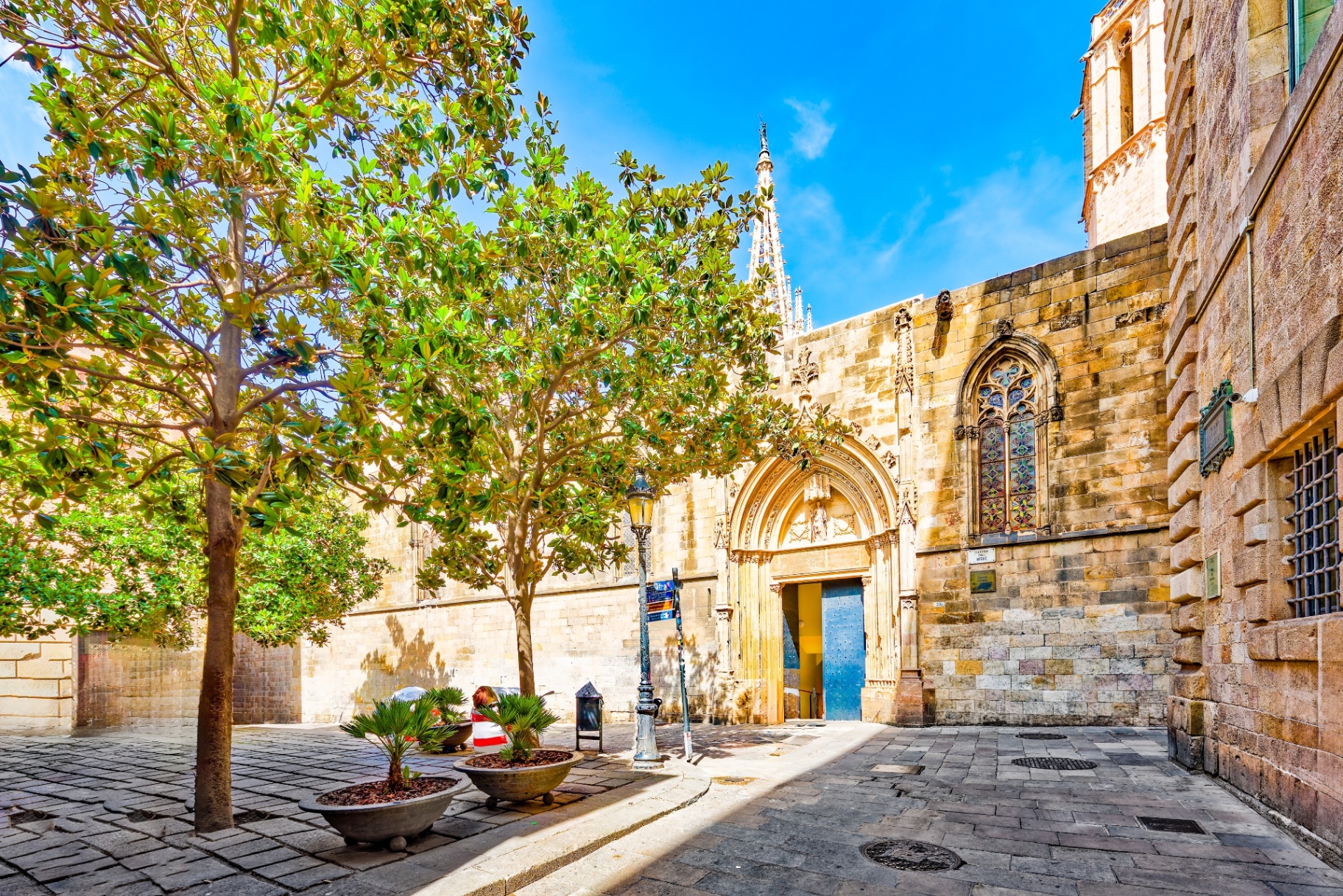 Historic Gothic Quarter courtyard with medieval stone walls, a blue door and Barcelona Cathedral spire in the background
