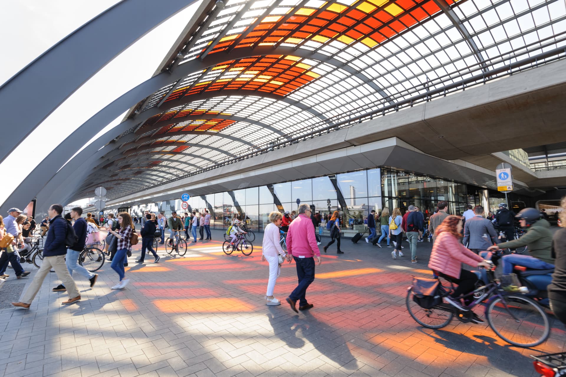 Pedestrians and cyclists under the coloured glass roof on the IJ side of Amsterdam Centraal Station