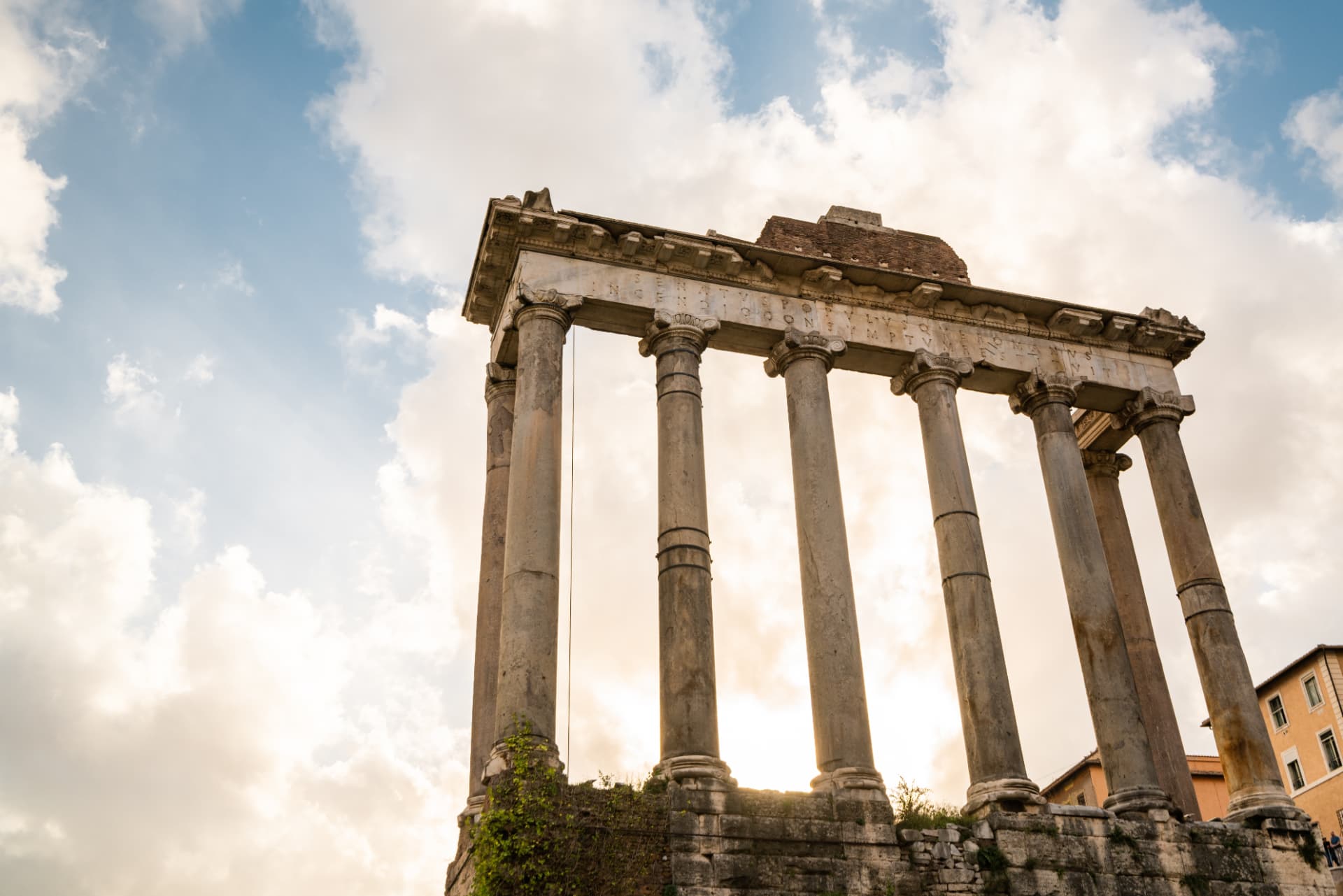 Eight granite columns and inscribed entablature of the Temple of Saturn against a bright sky