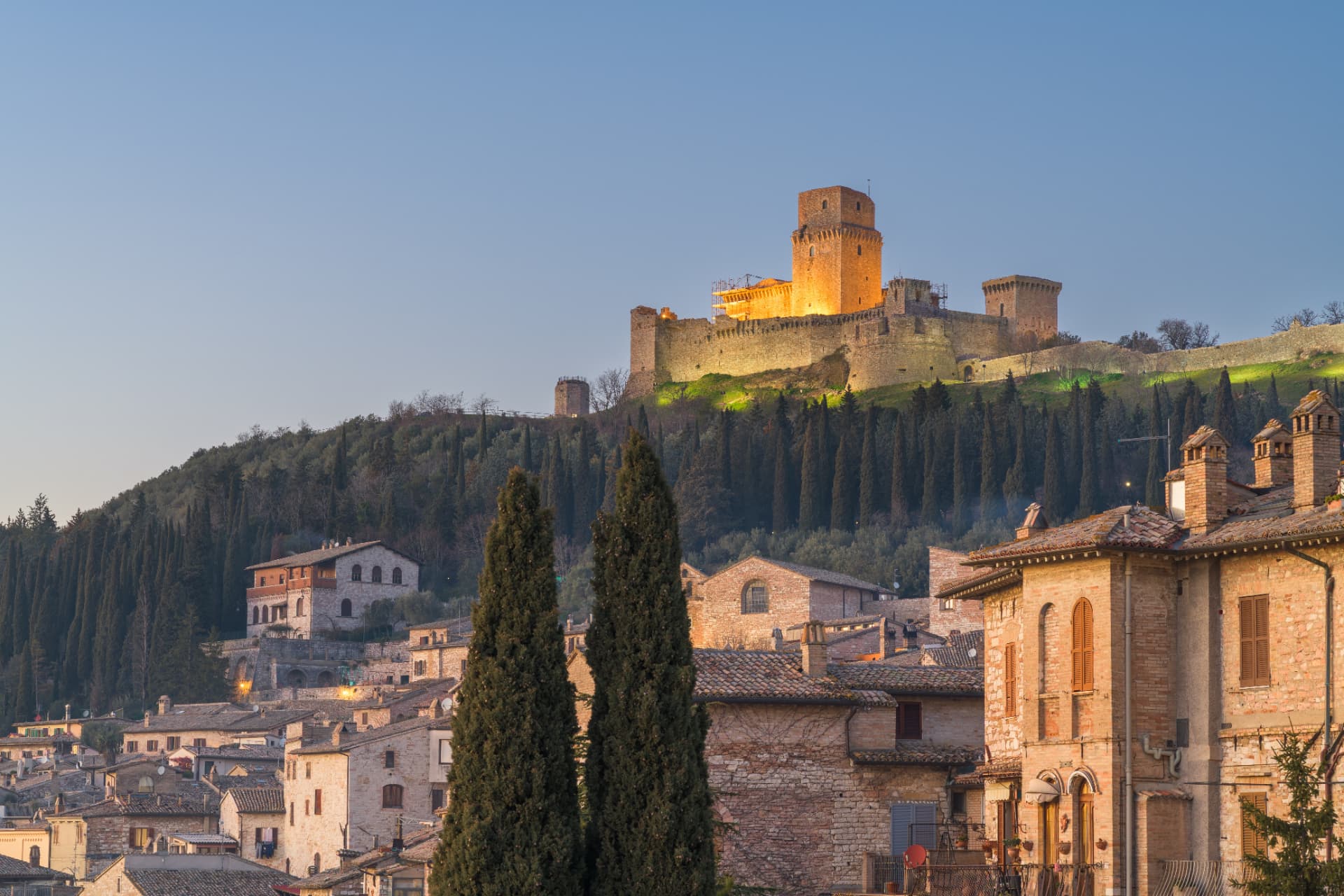 The floodlit Rocca Maggiore fortress on the hill above Assisi's rooftops at dusk