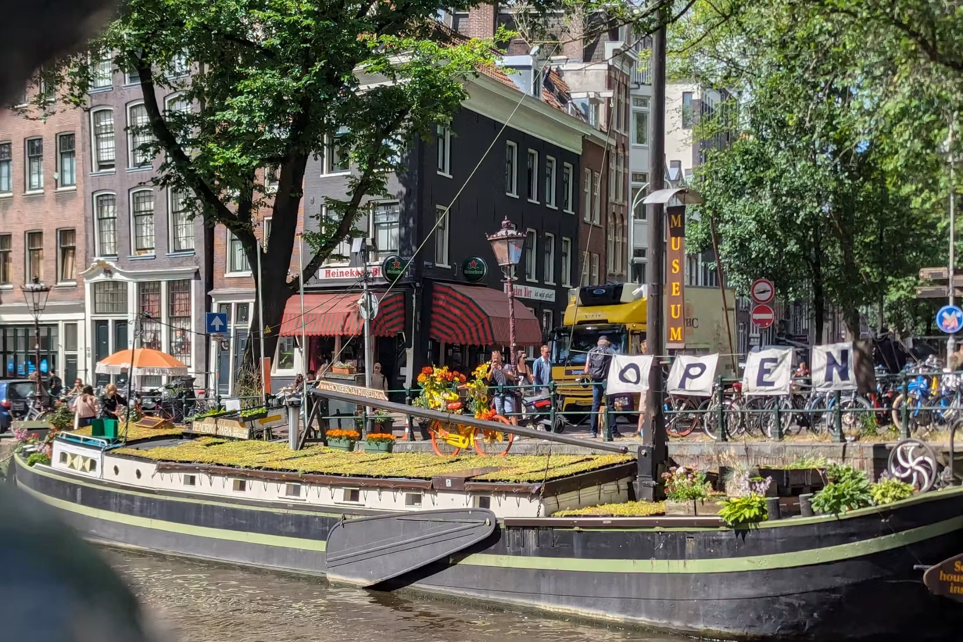 The Houseboat Museum barge on the Prinsengracht in Amsterdam with plants growing on its deck and an open sign