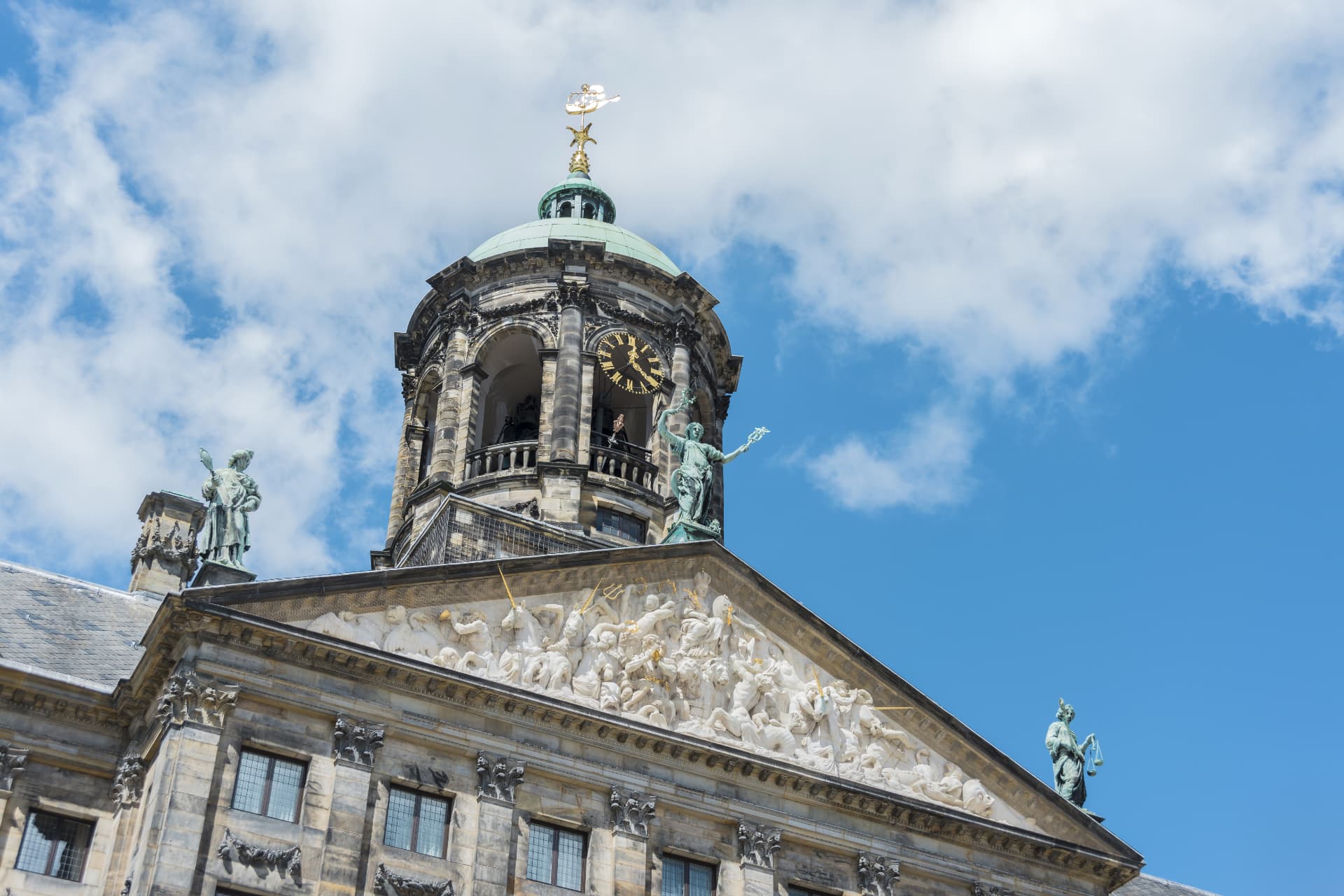 The domed tower and sculpted pediment of the Royal Palace of Amsterdam against a blue sky