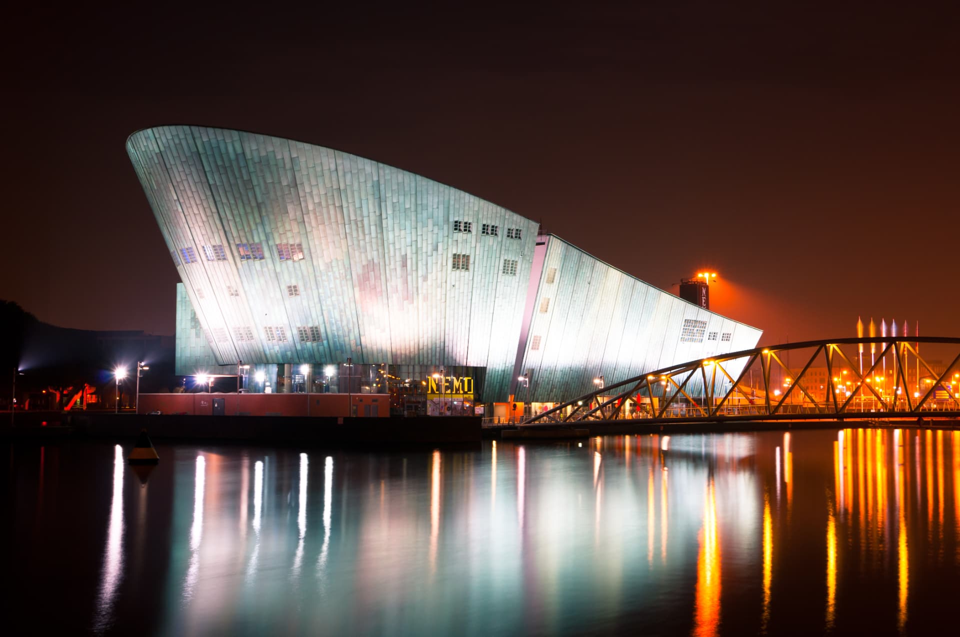 The NEMO Science Museum building in Amsterdam illuminated at night and reflected in the harbour water