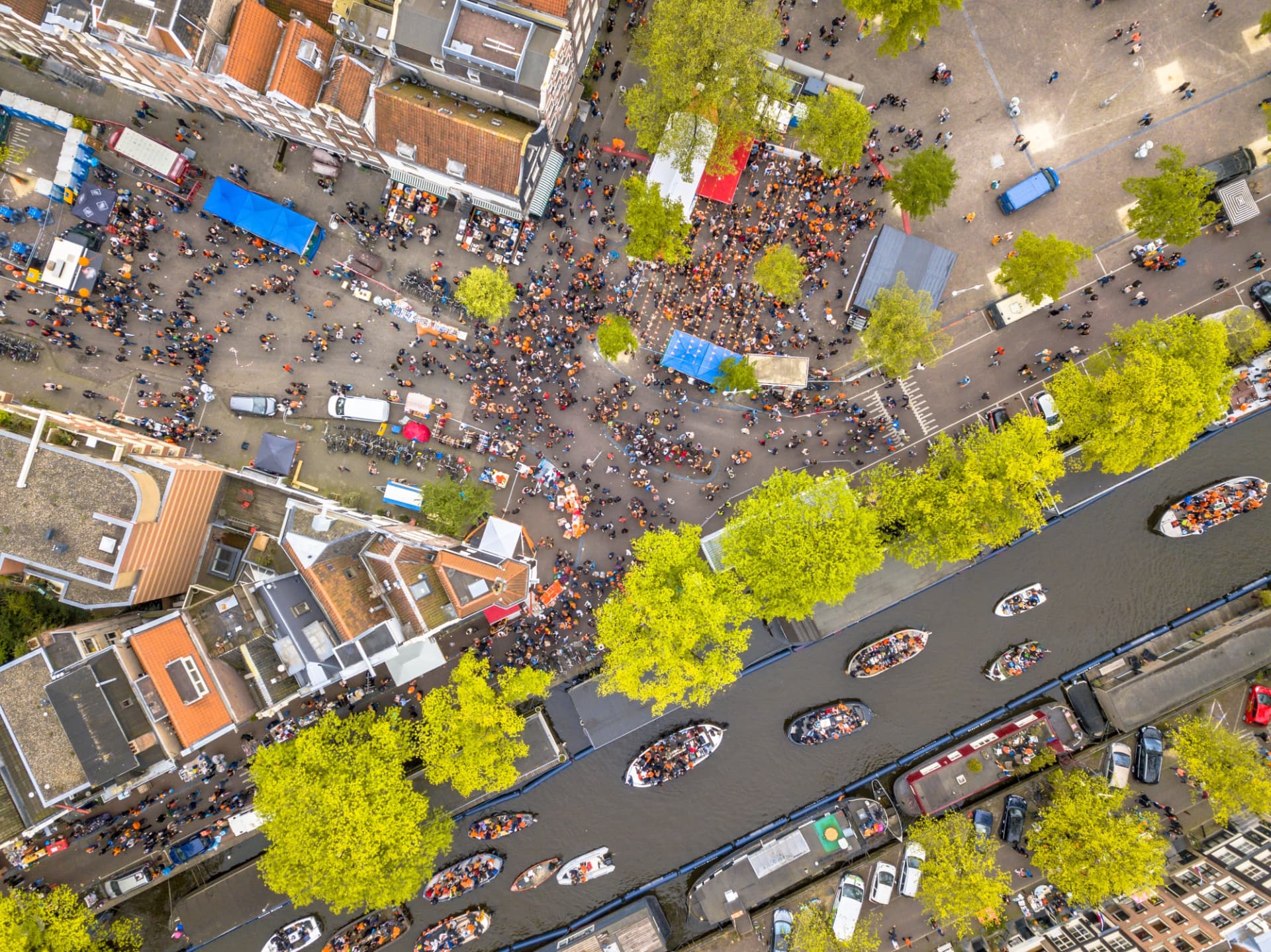 Aerial view of crowds in orange around a square and boats on the Prinsengracht canal in Amsterdam on King's Day