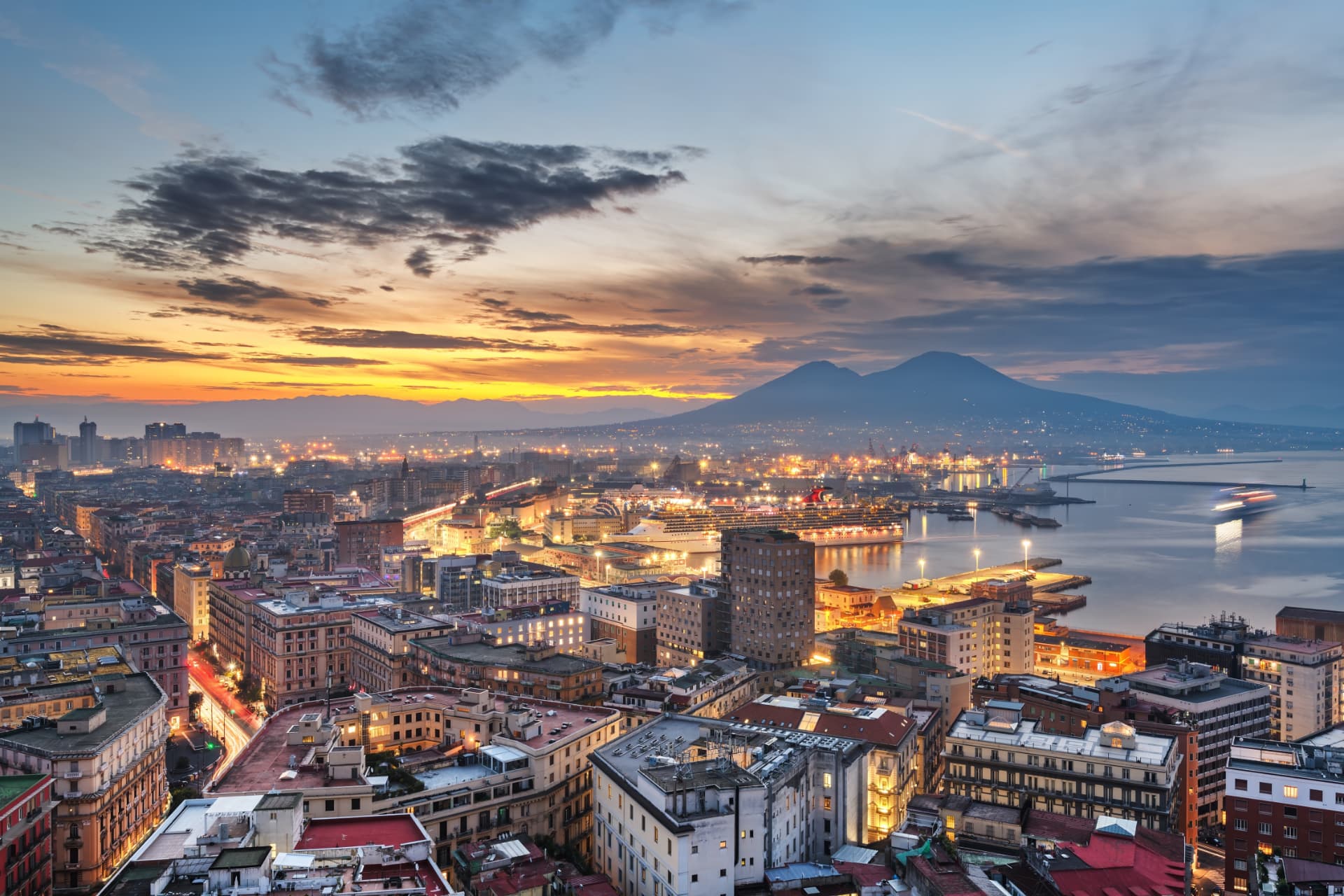 Naples at dusk with the city lights, the port and Mount Vesuvius across the bay