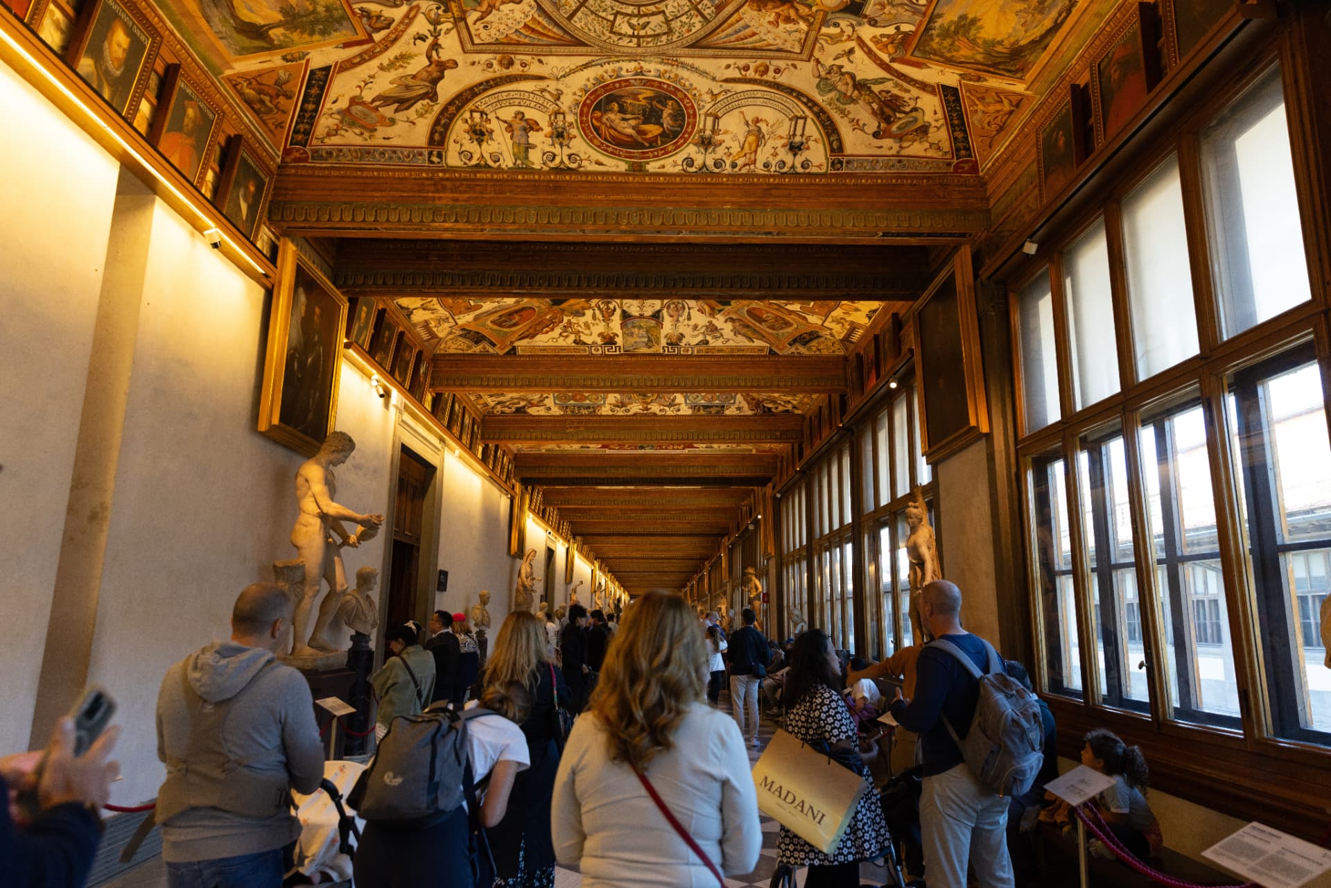 Visitors beneath the decorated ceiling of an Uffizi sculpture corridor