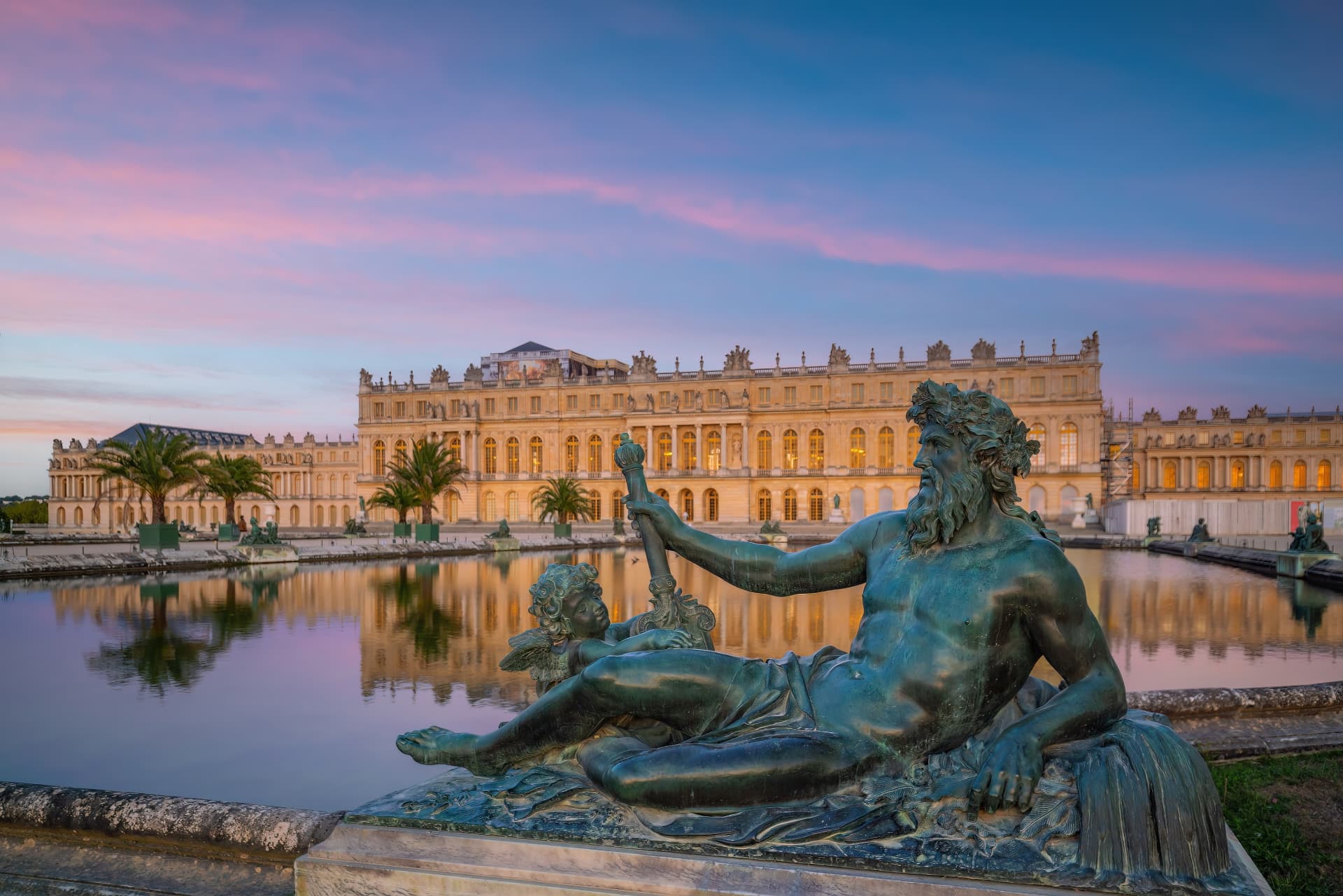 Bronze sculpture beside the Neptune Fountain at twilight with the Palace of Versailles reflected behind