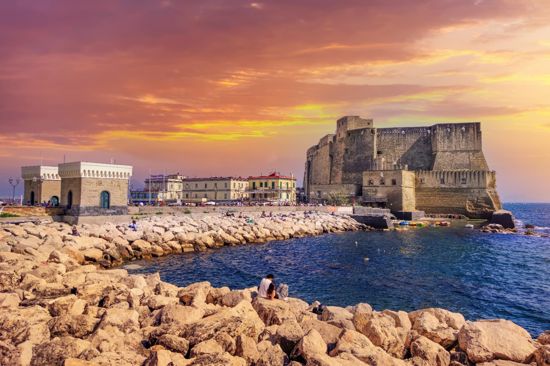 Castel dell'Ovo on the Naples waterfront at sunset, seen from the rocky shore