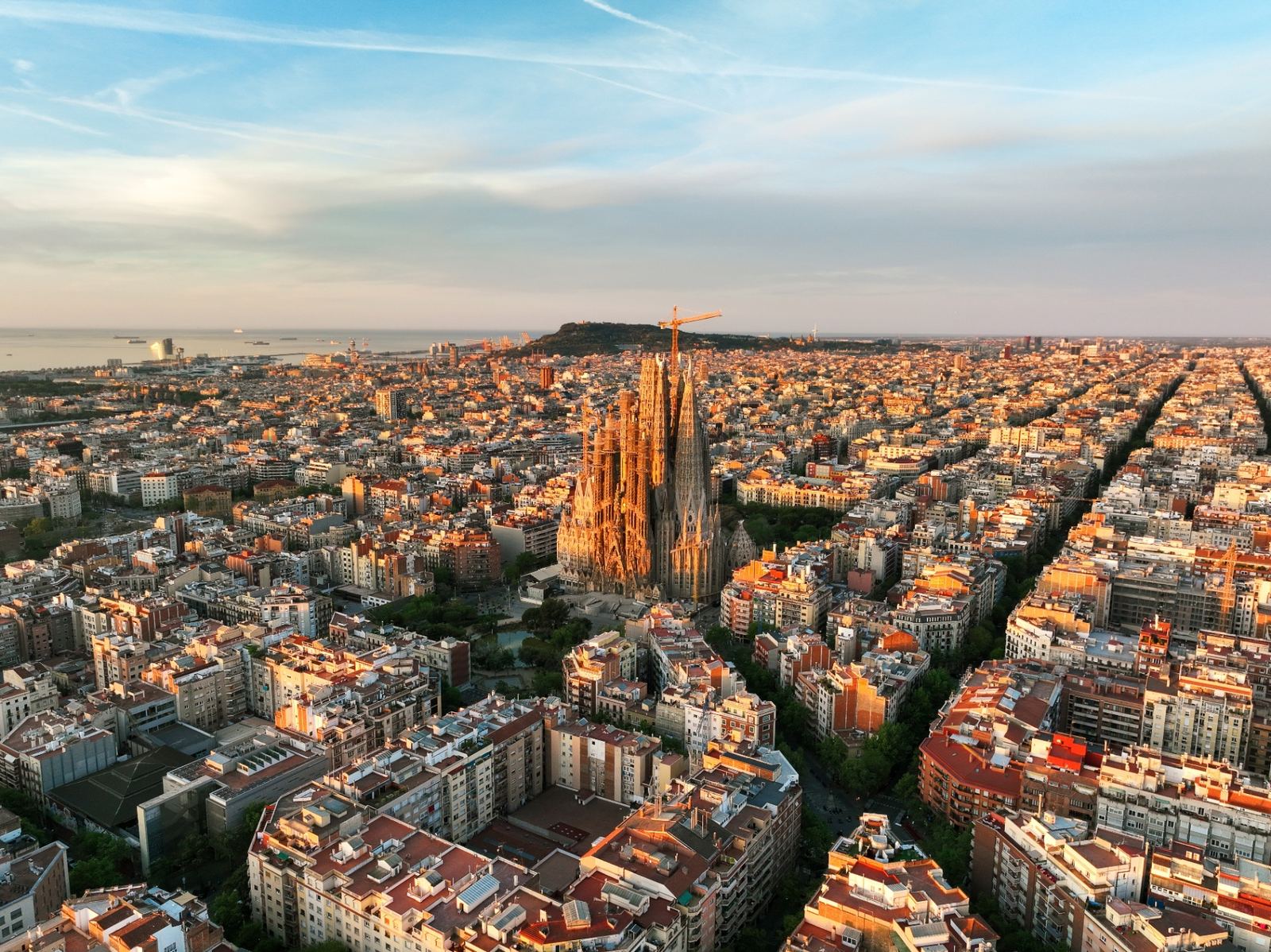 Barcelona skyline at sunset with Sagrada Família rising above the city and the Mediterranean coast in the distance
