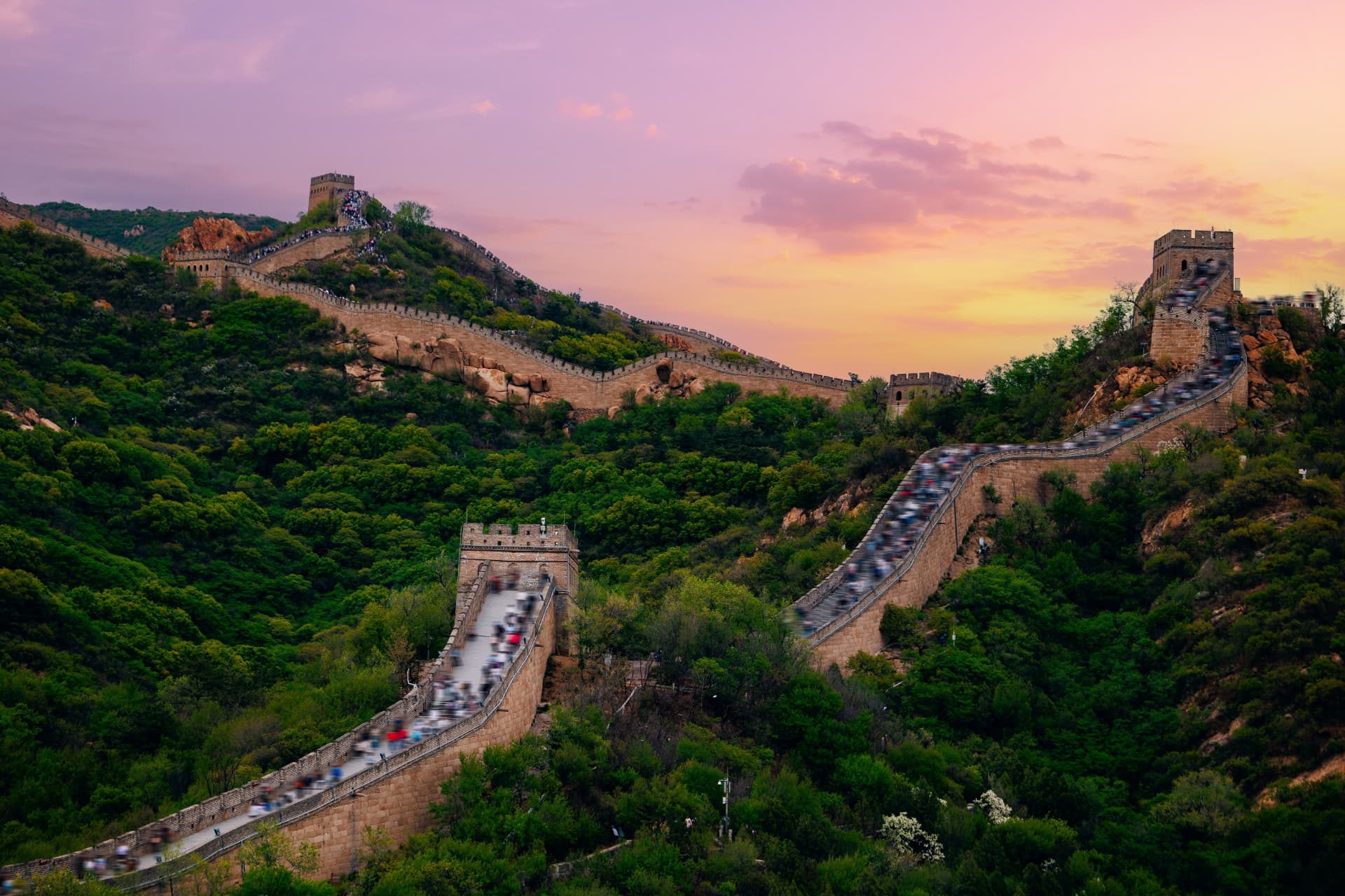 Long queues of visitors packed along the Great Wall's steps and towers at dusk under a pink sky