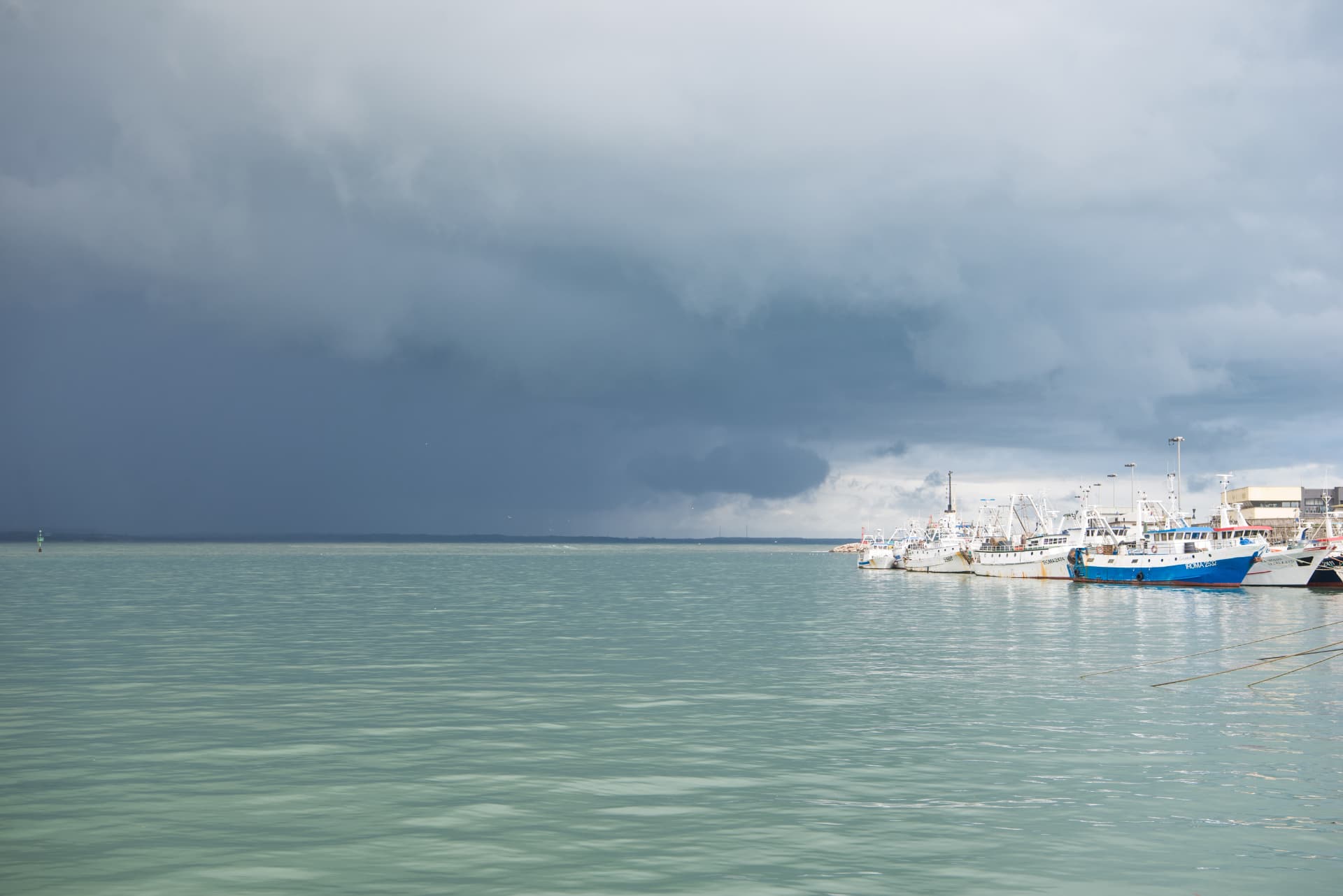 Fishing boats moored in Anzio harbour beneath approaching storm clouds