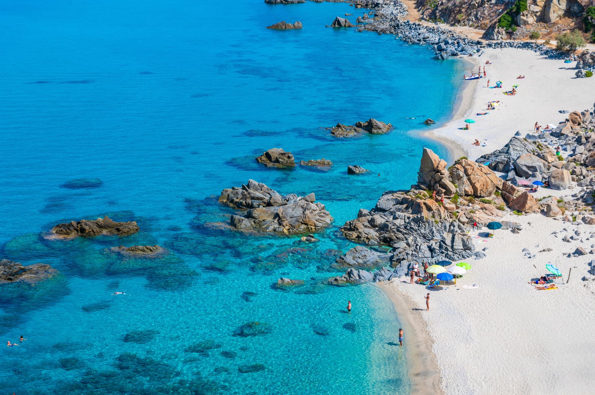 A small rocky cove with white sand, colourful umbrellas and clear turquoise water on the Lazio coast