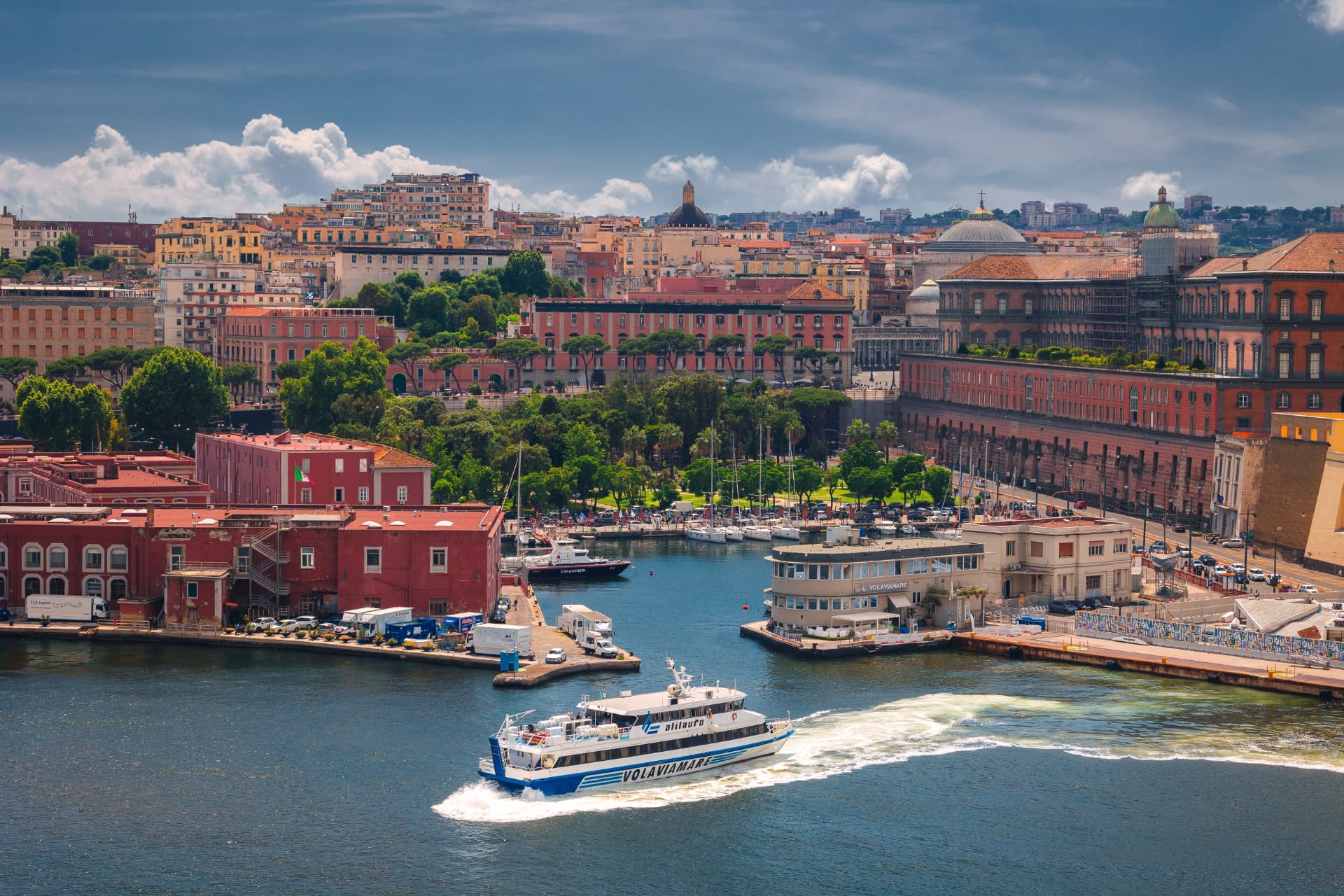 A Volaviamare passenger ferry crossing the harbour in front of Naples' waterfront buildings and moored boats