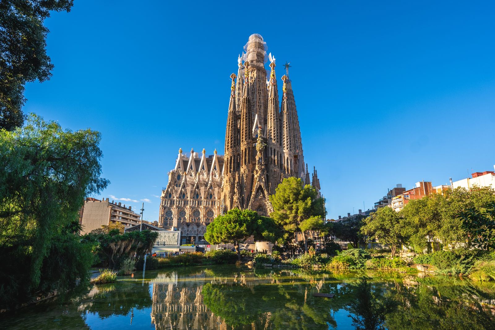 Sagrada Família basilica reflected in the pond of Gaudí Square under a clear blue Barcelona sky