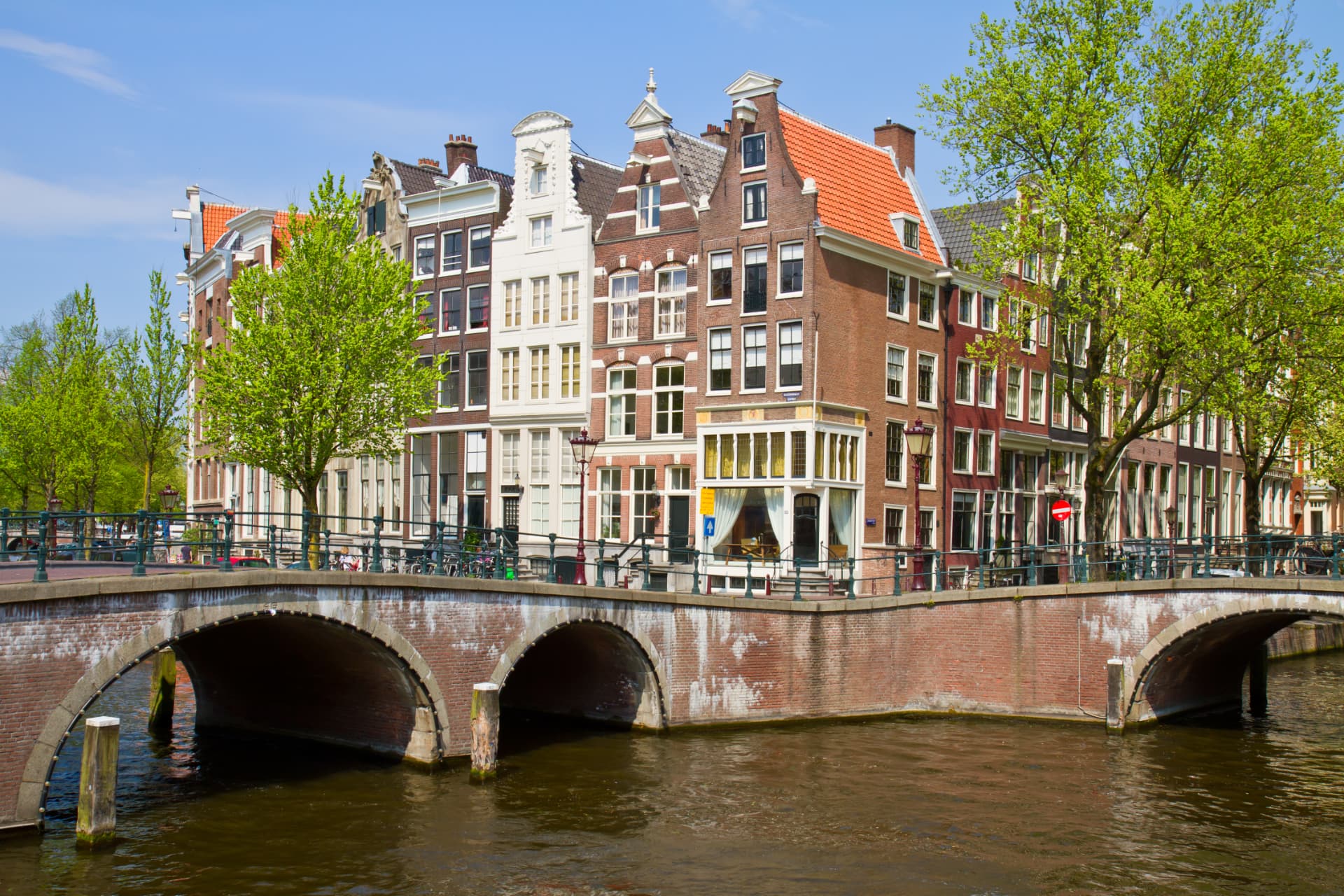 Gabled 17th-century merchant houses along a canal in Amsterdam's Grachtengordel with a brick bridge in the foreground